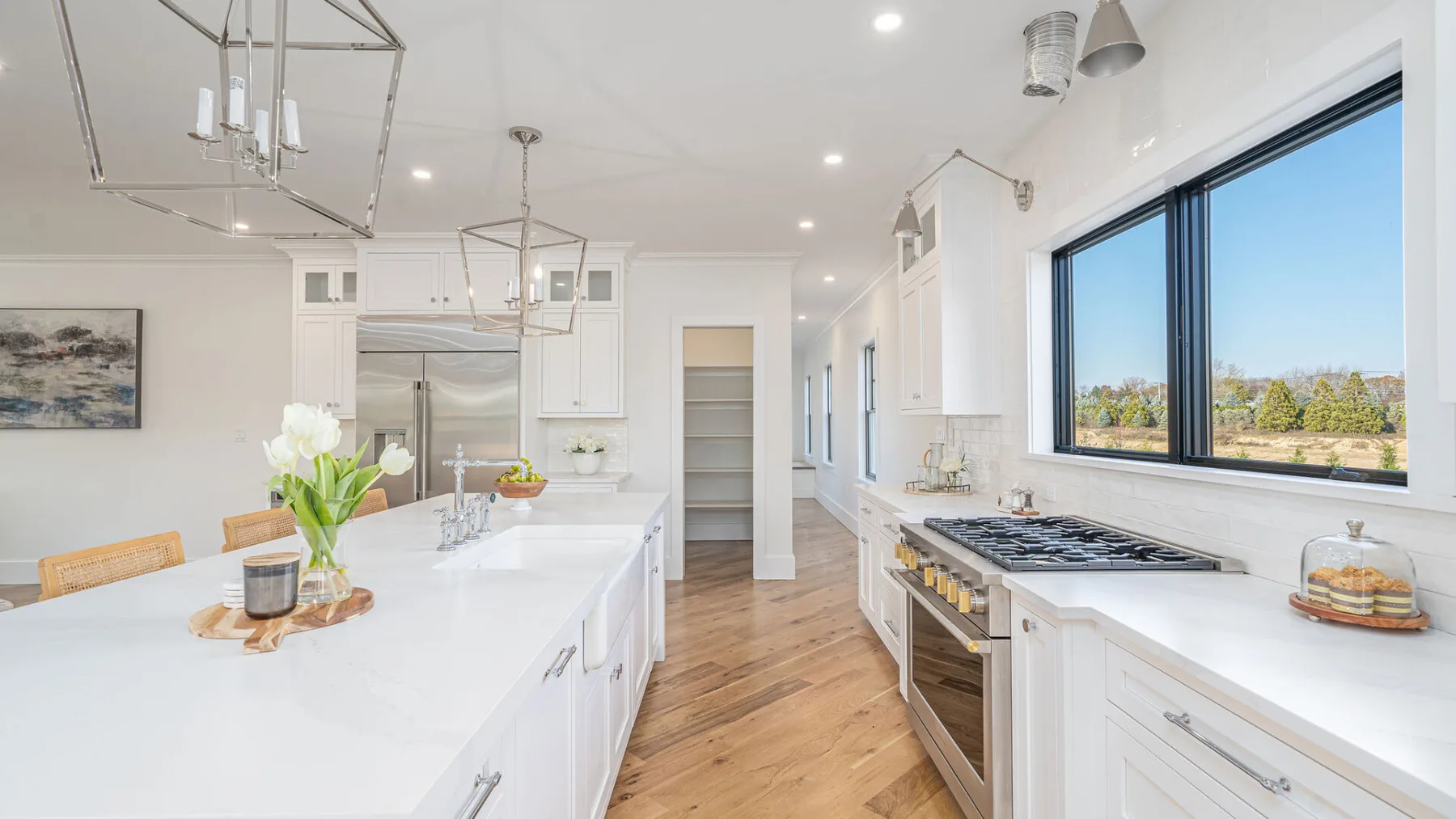 A bright kitchen with white counters, wood flooring, and a large window.
