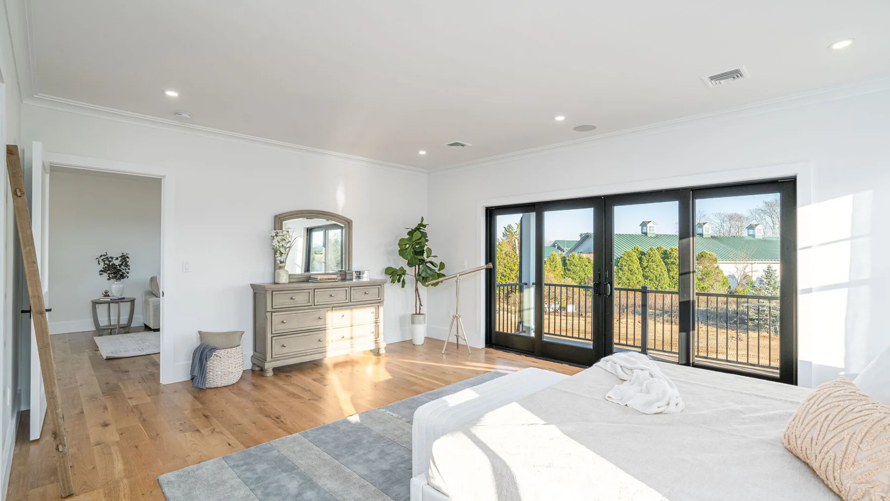 A bright bedroom with a large bed and black-framed glass doors.