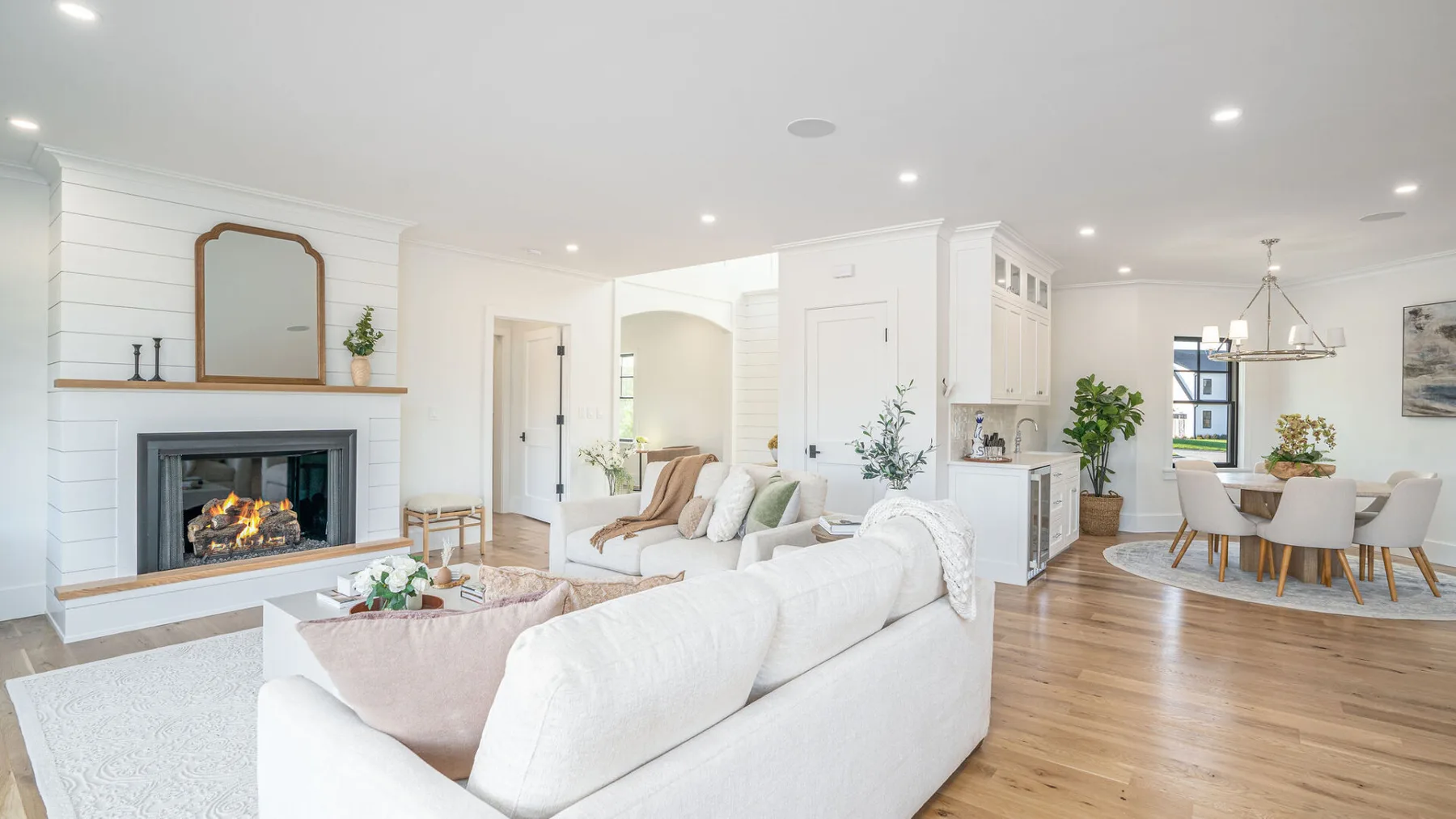 An open-plan living room with white seating, a fireplace, and a dining area.