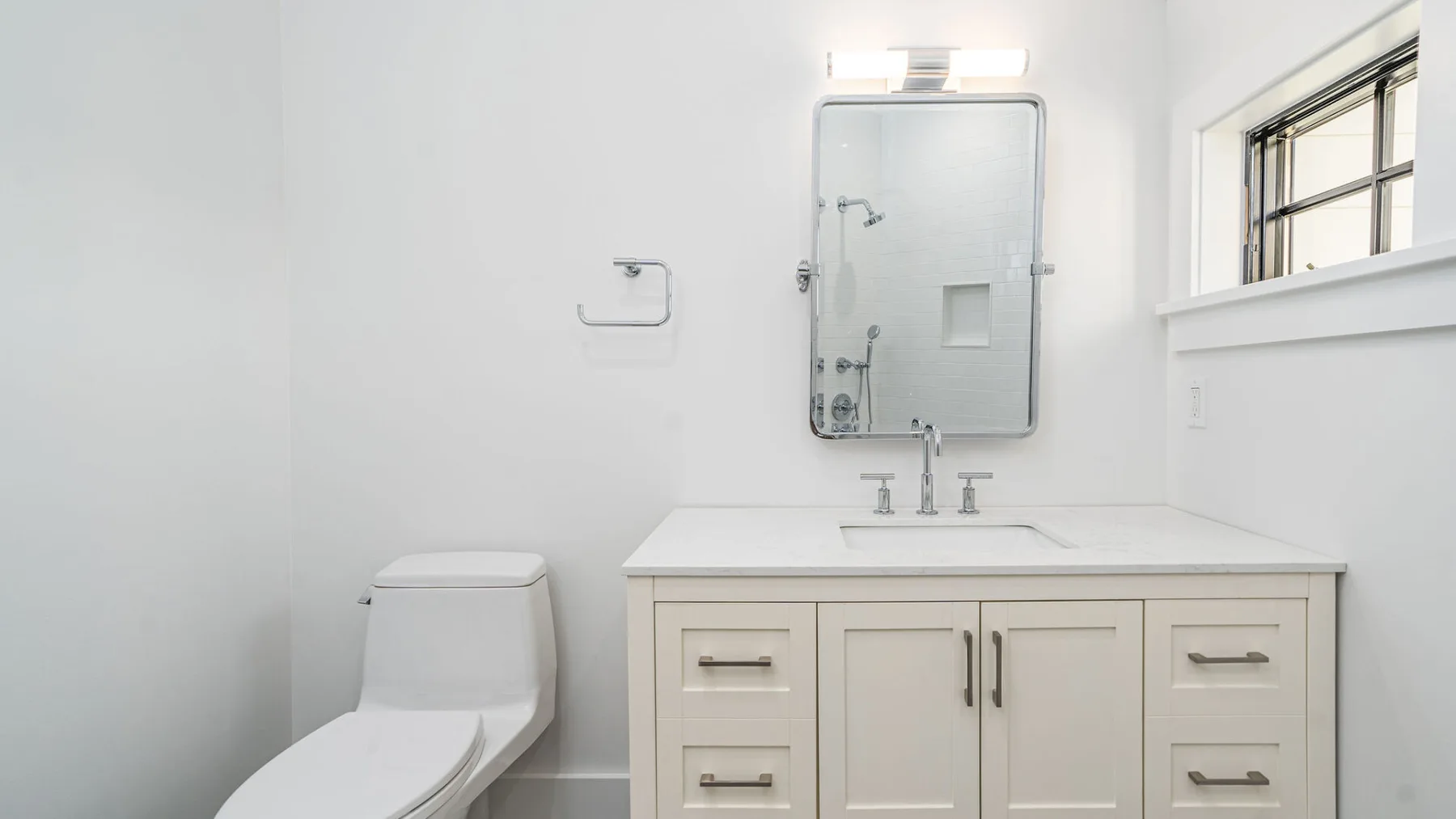 A bright bathroom with a vanity, mirror, toilet, and window.