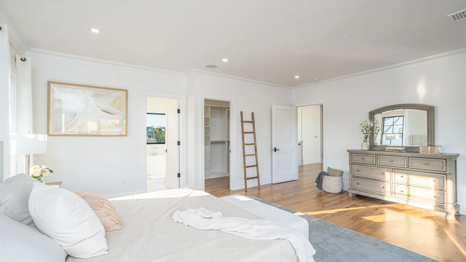 A bright bedroom with a bed, dresser, and mirror.