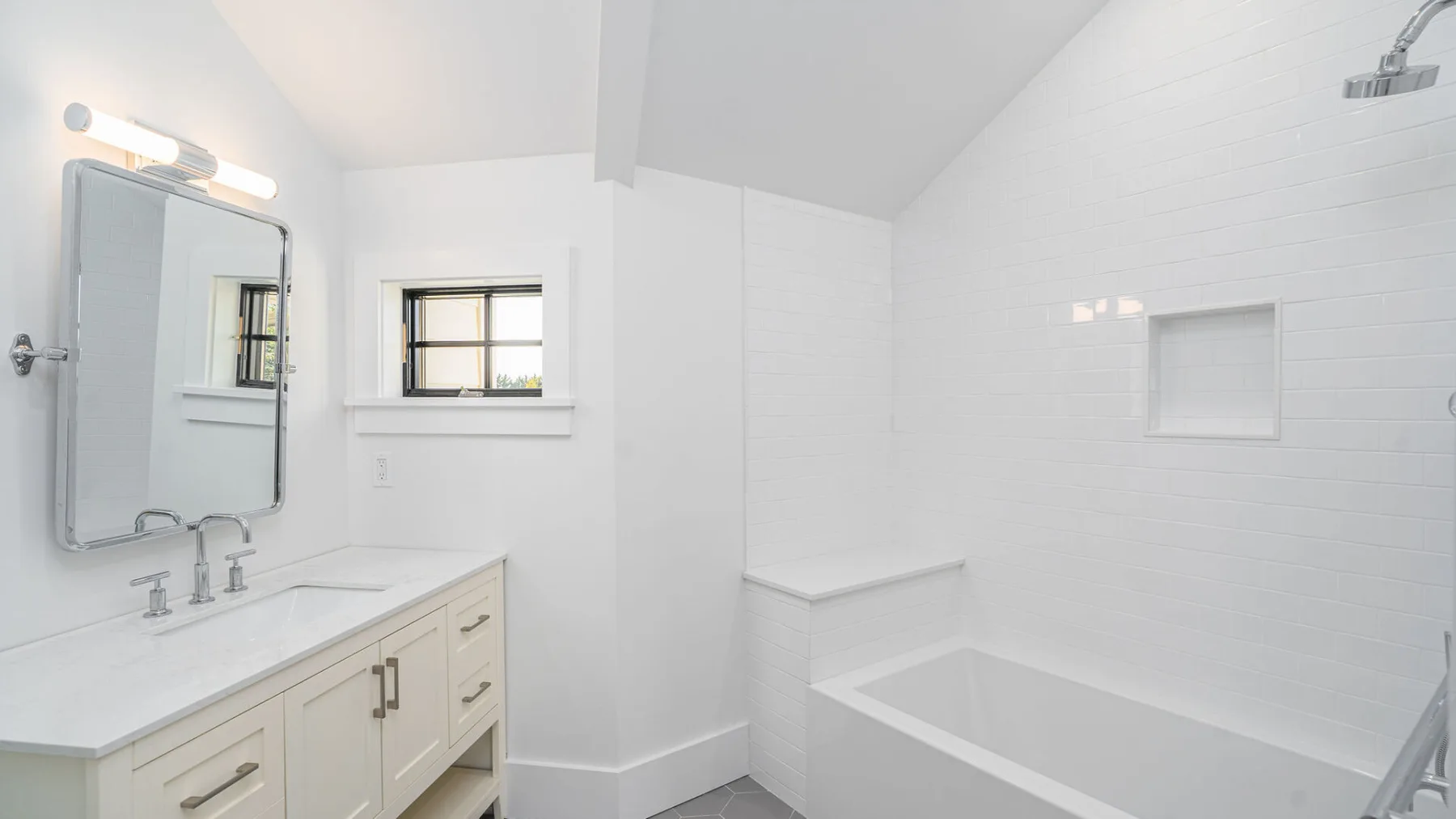 A bright bathroom with a vanity, mirror, and bathtub.