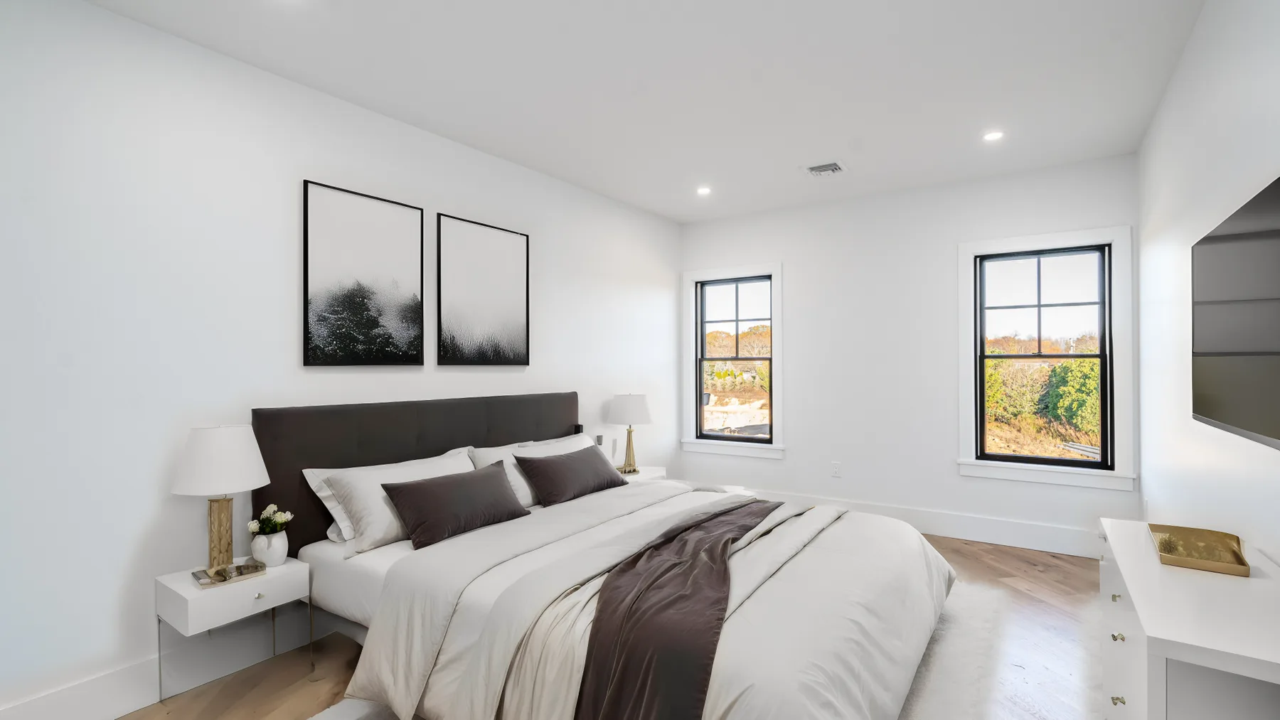 A bright bedroom with a neatly made bed and two large windows.