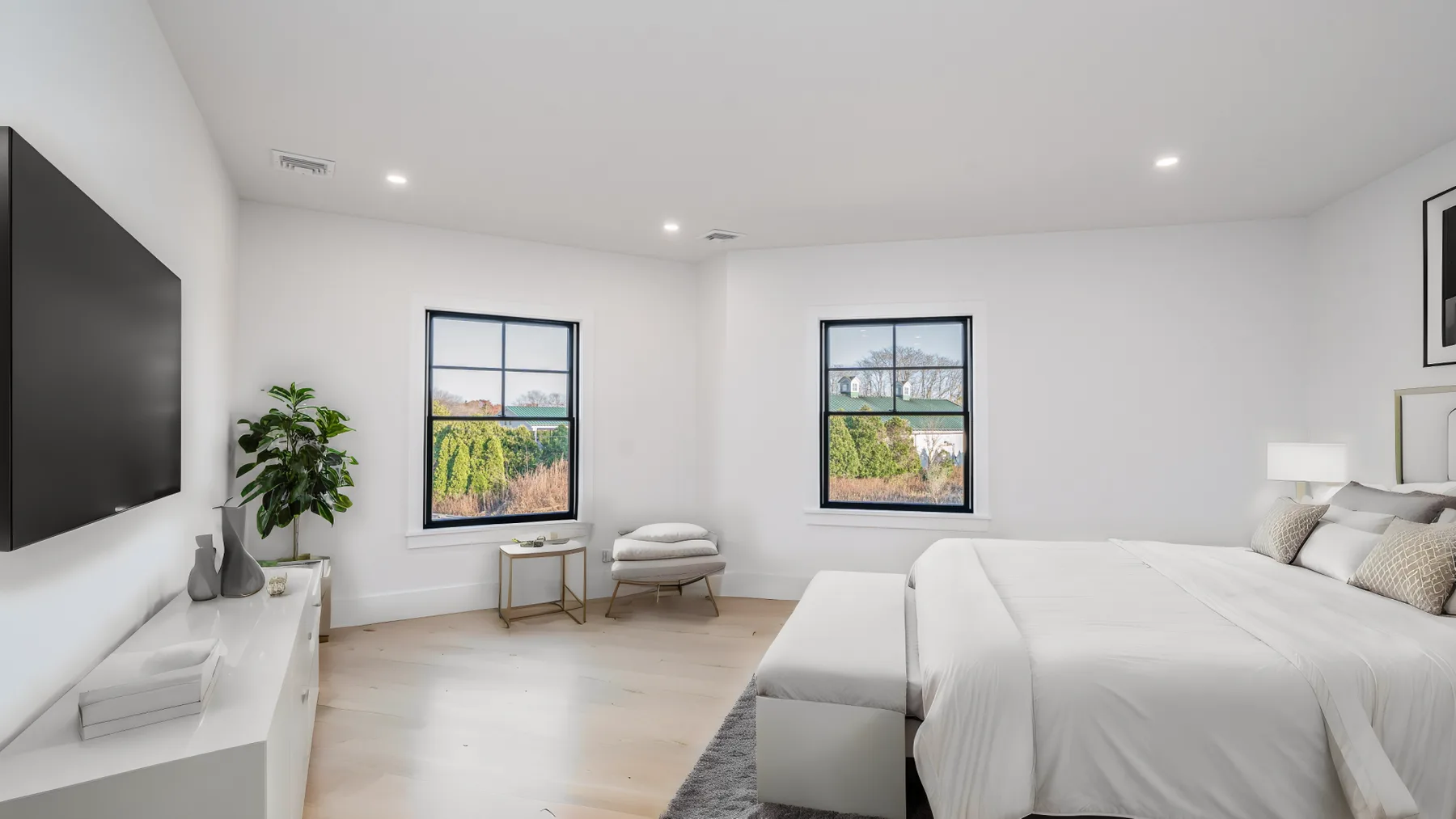 A bright bedroom with a bed, television, and two windows.