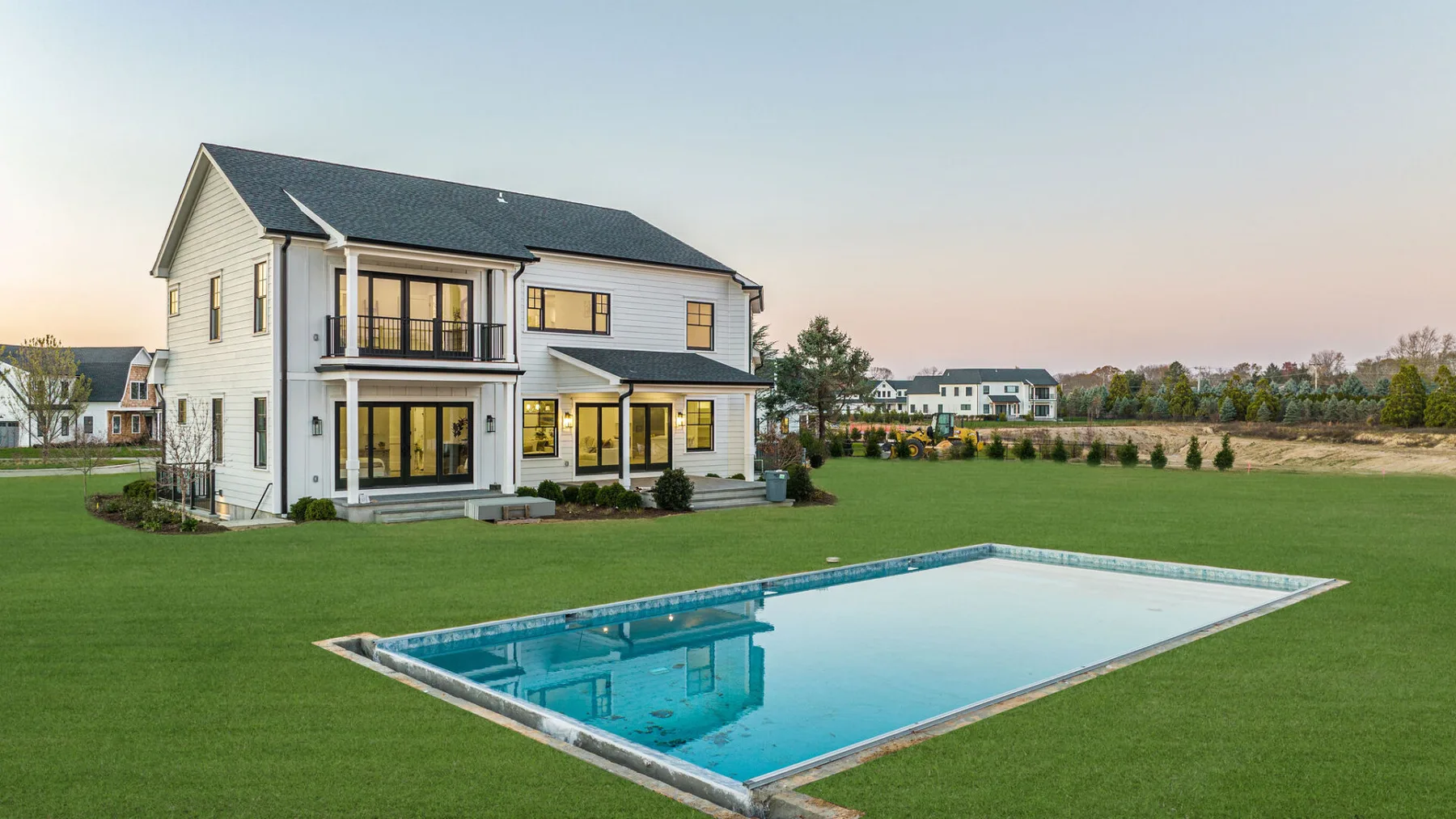 A large two-story house stands beside a rectangular outdoor swimming pool on a lawn.