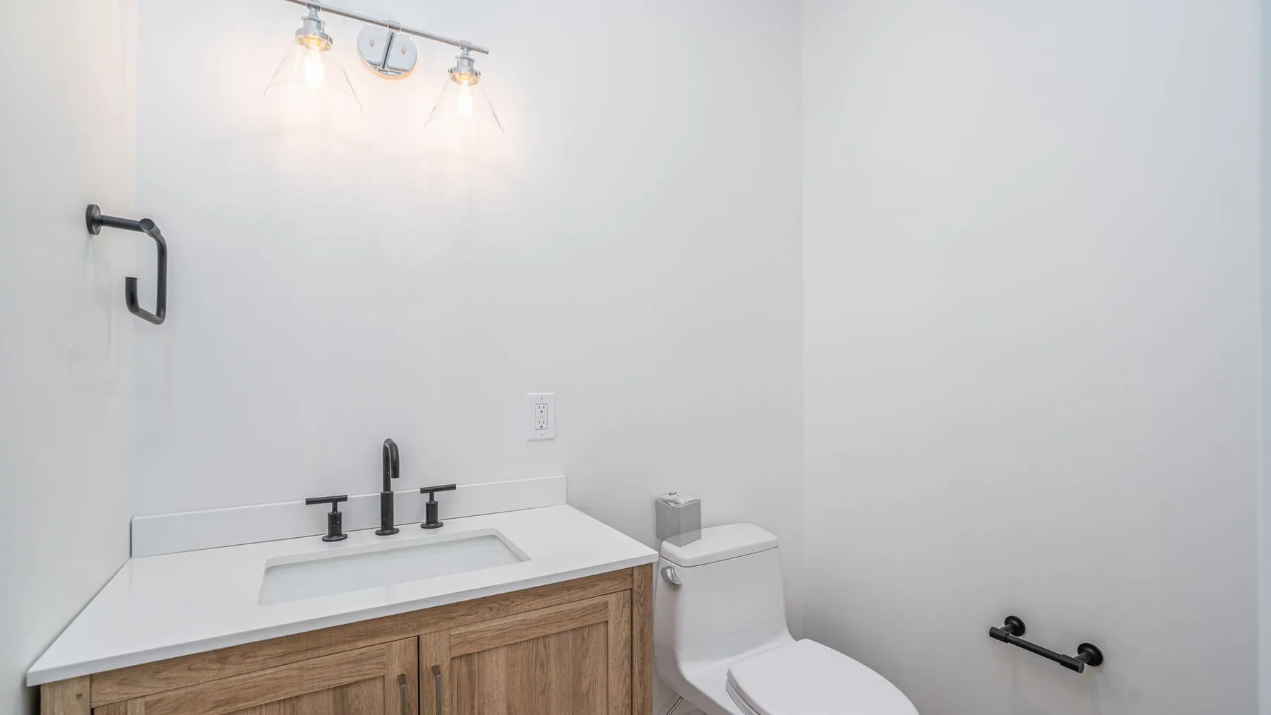 A bathroom vanity with a sink, toilet, and wall-mounted grab bars.