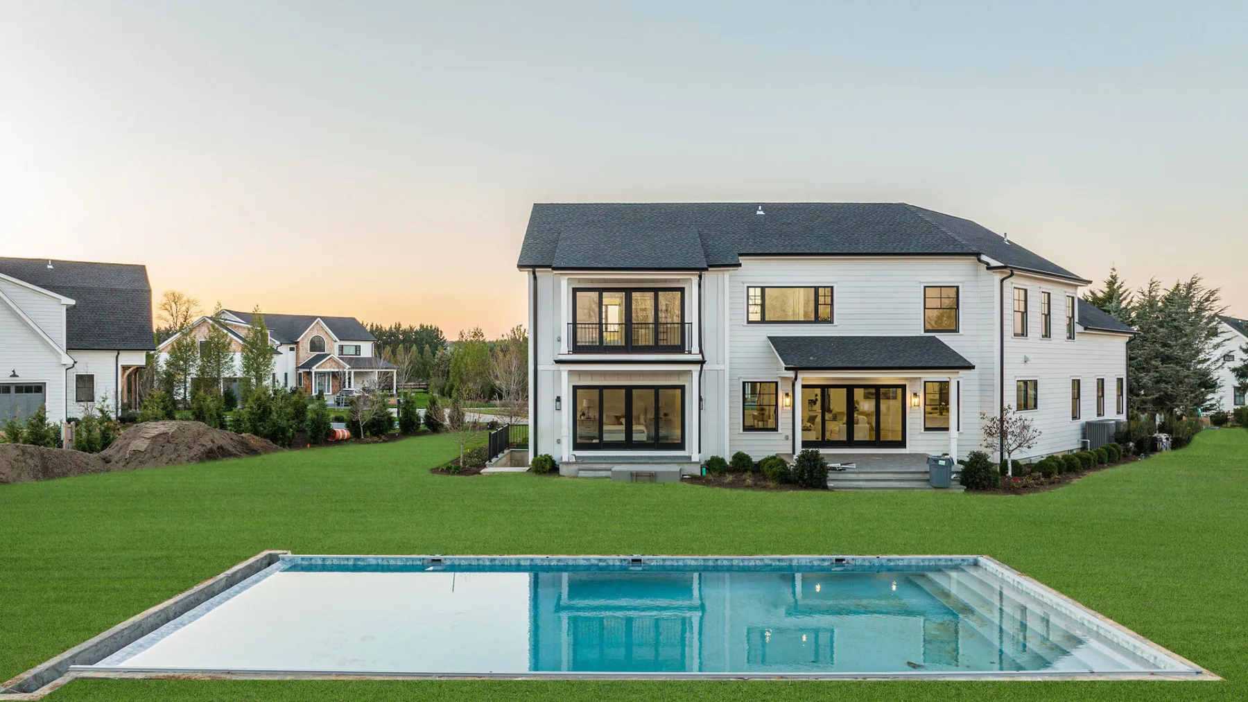 A large modern house stands behind a rectangular swimming pool and lawn.