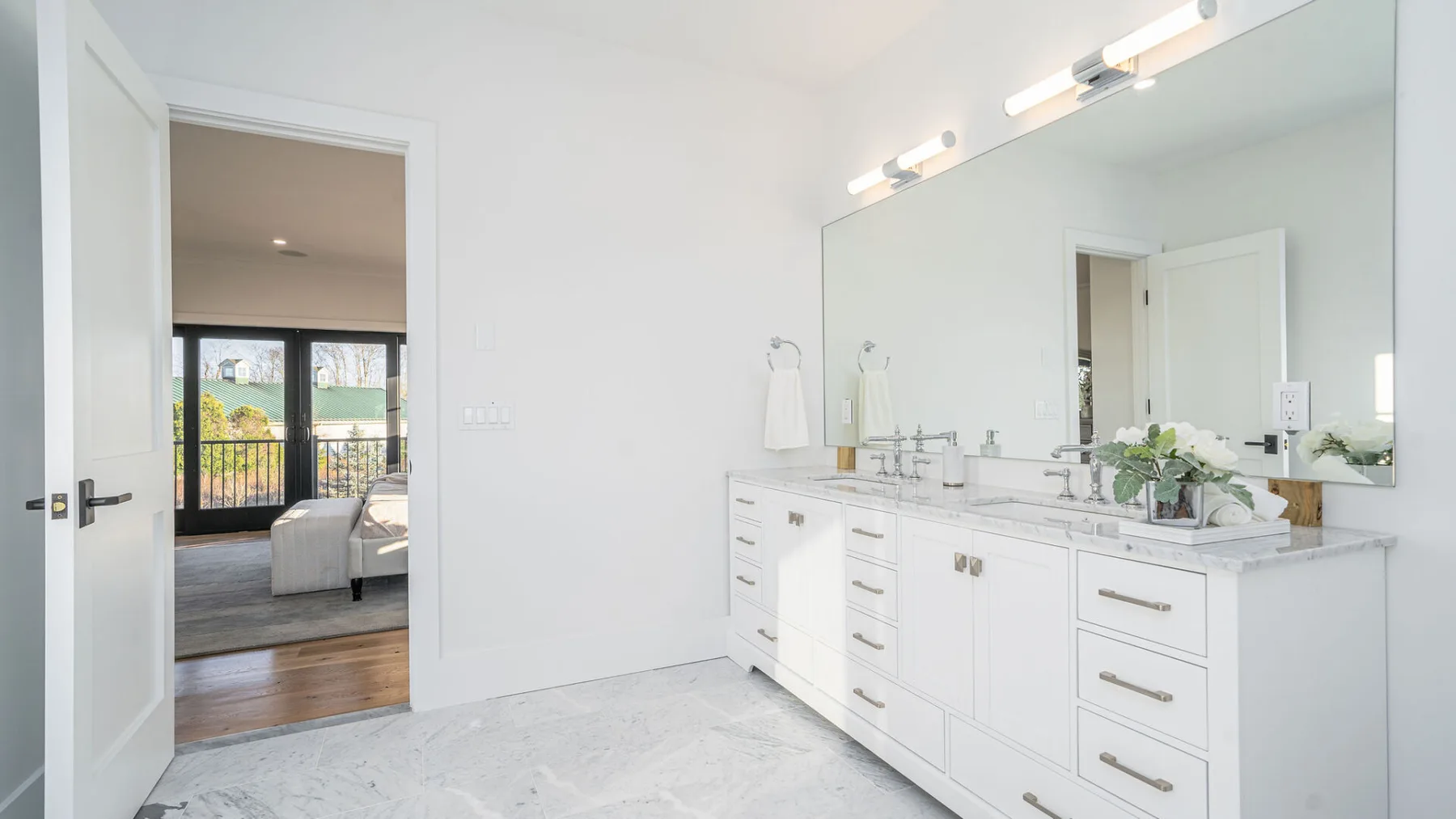 A bright bathroom features a long white vanity beneath a large mirror.