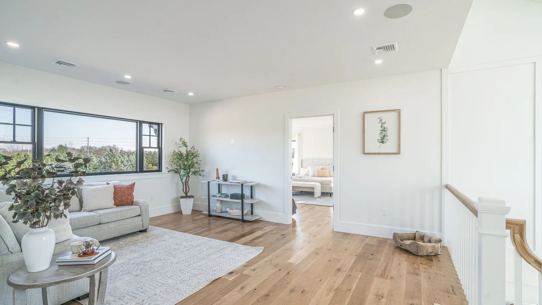 A bright living room with a sofa, large windows, and light wood flooring.