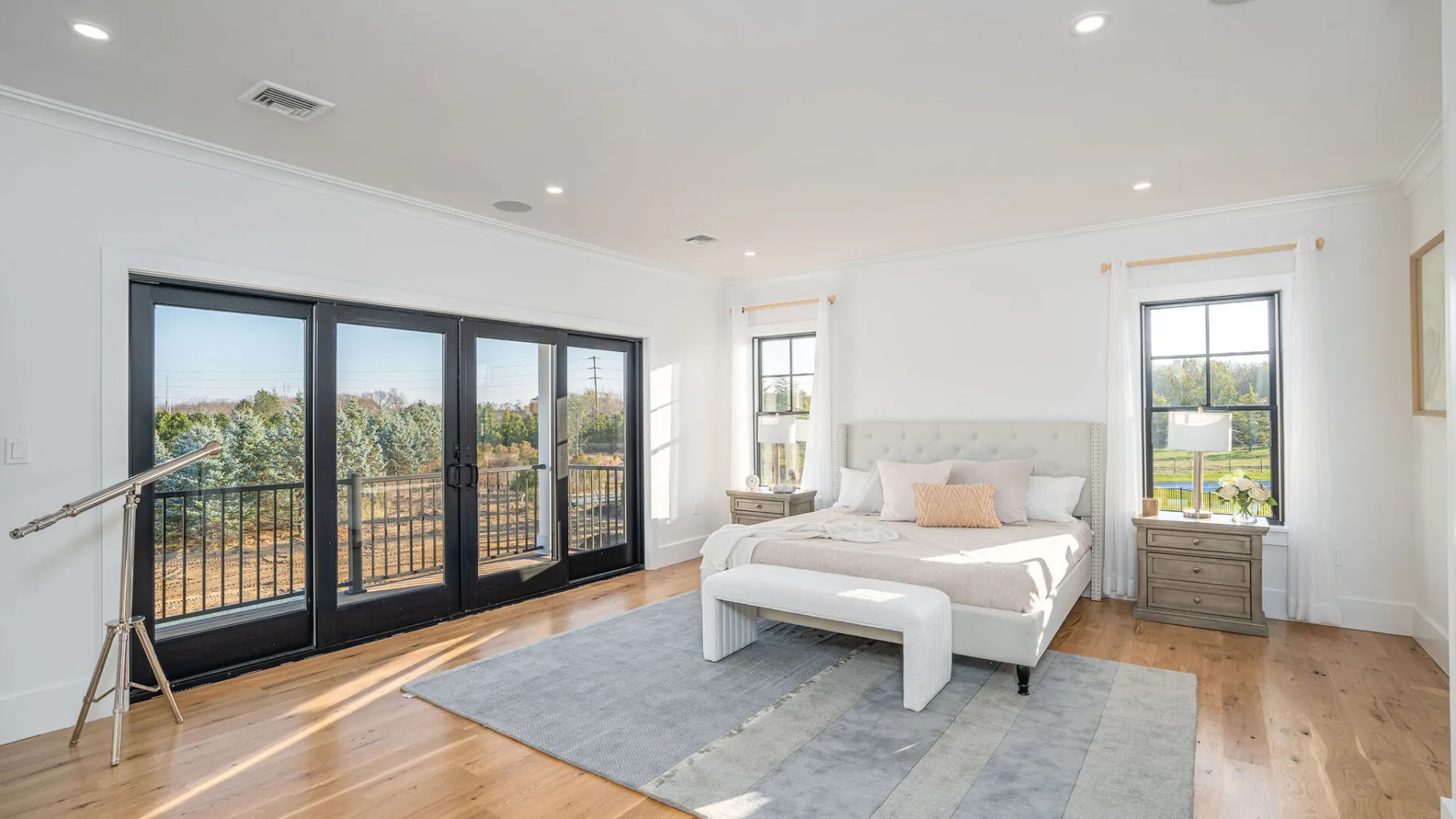 A bright bedroom with a bed, a rug, and large windows opening onto a balcony.
