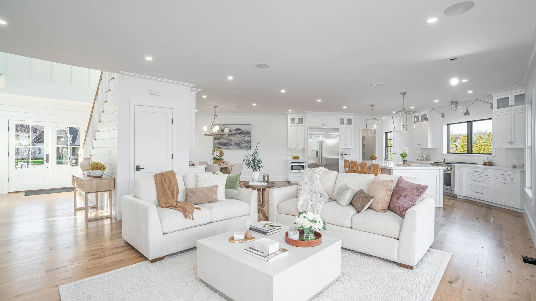 A bright open-plan living room and kitchen with white seating and cabinetry.