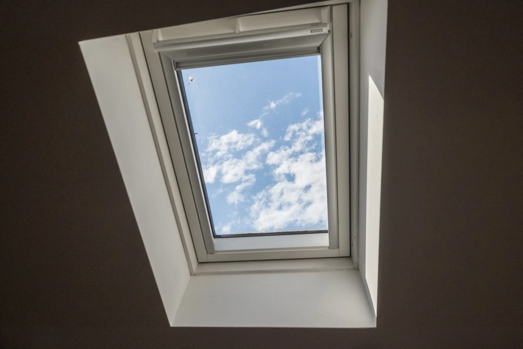 Una claraboya en un techo inclinado muestra un cielo azul con nubes dispersas.
