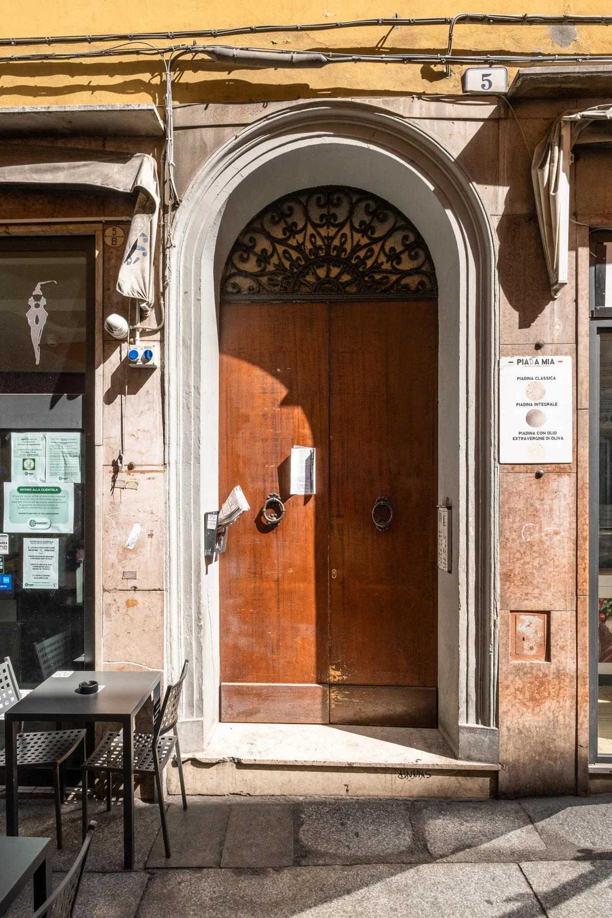 Una alta puerta de madera se encuentra bajo un marco de piedra arqueado en la fachada de un edificio.