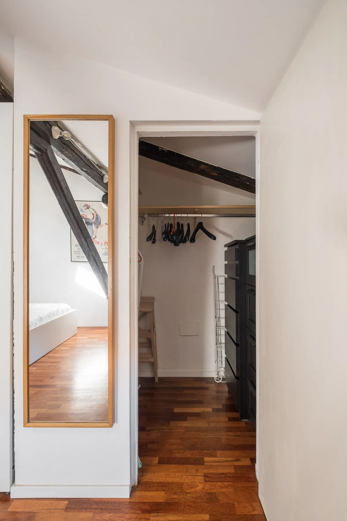 Un pasillo de paredes blancas da a un vestidor con ropa colgada.