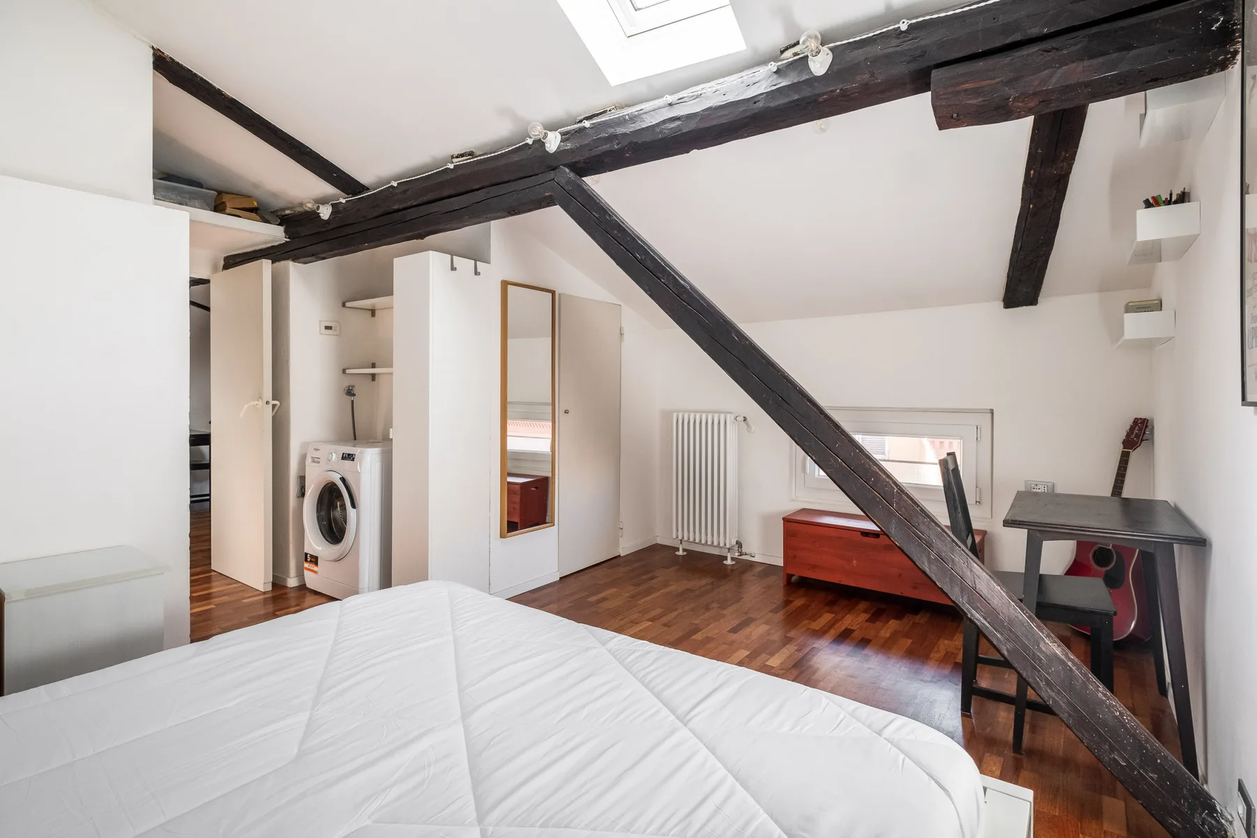 Un dormitorio con una cama, vigas oscuras a la vista y un escritorio pequeño.
