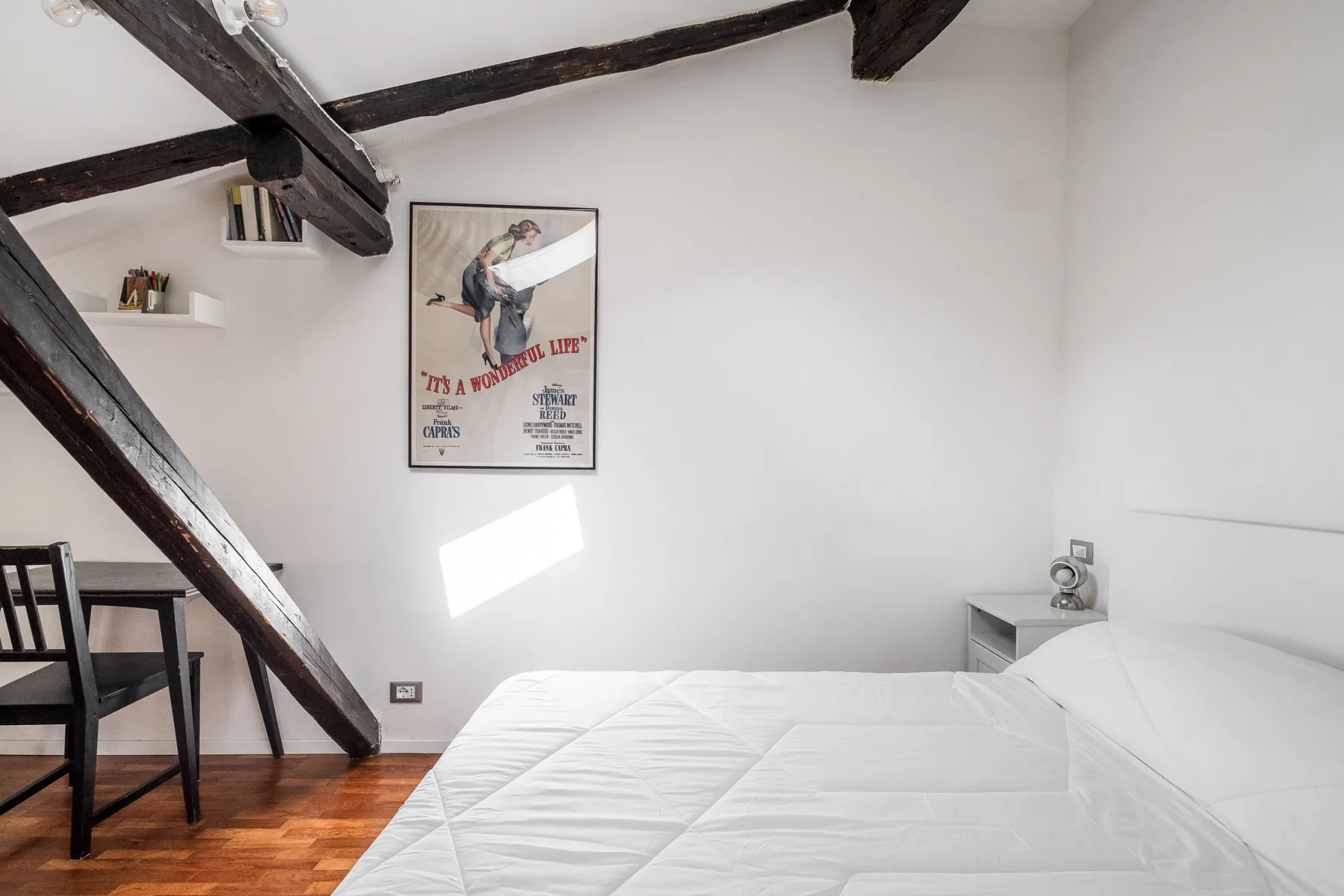 Un dormitorio con una cama, vigas oscuras en el techo y un cartel enmarcado.