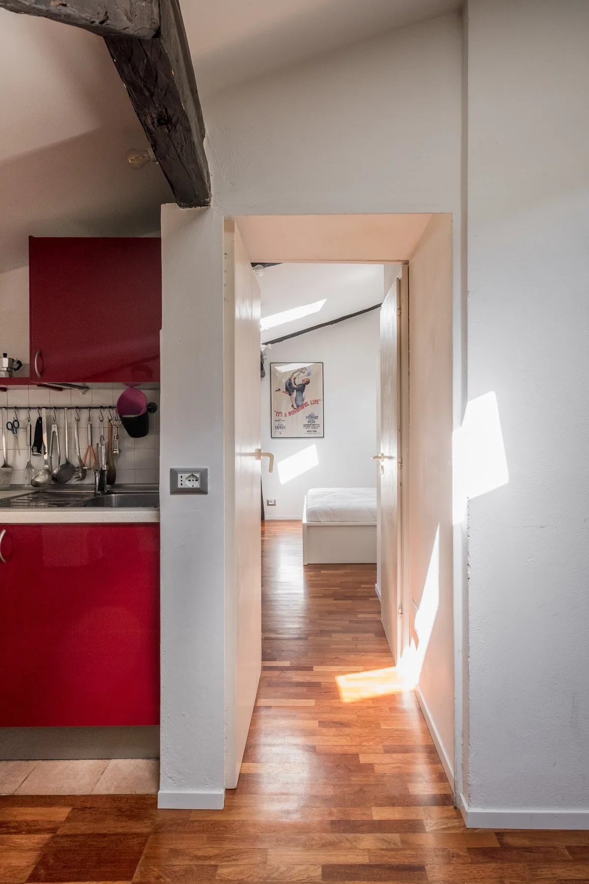 Un pasillo da a un dormitorio, con una cocina roja visible a la izquierda.