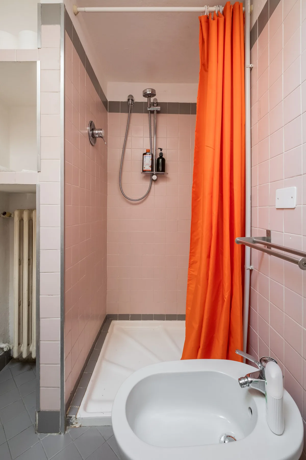 Un baño con azulejos, ducha, cortina naranja y lavabo.