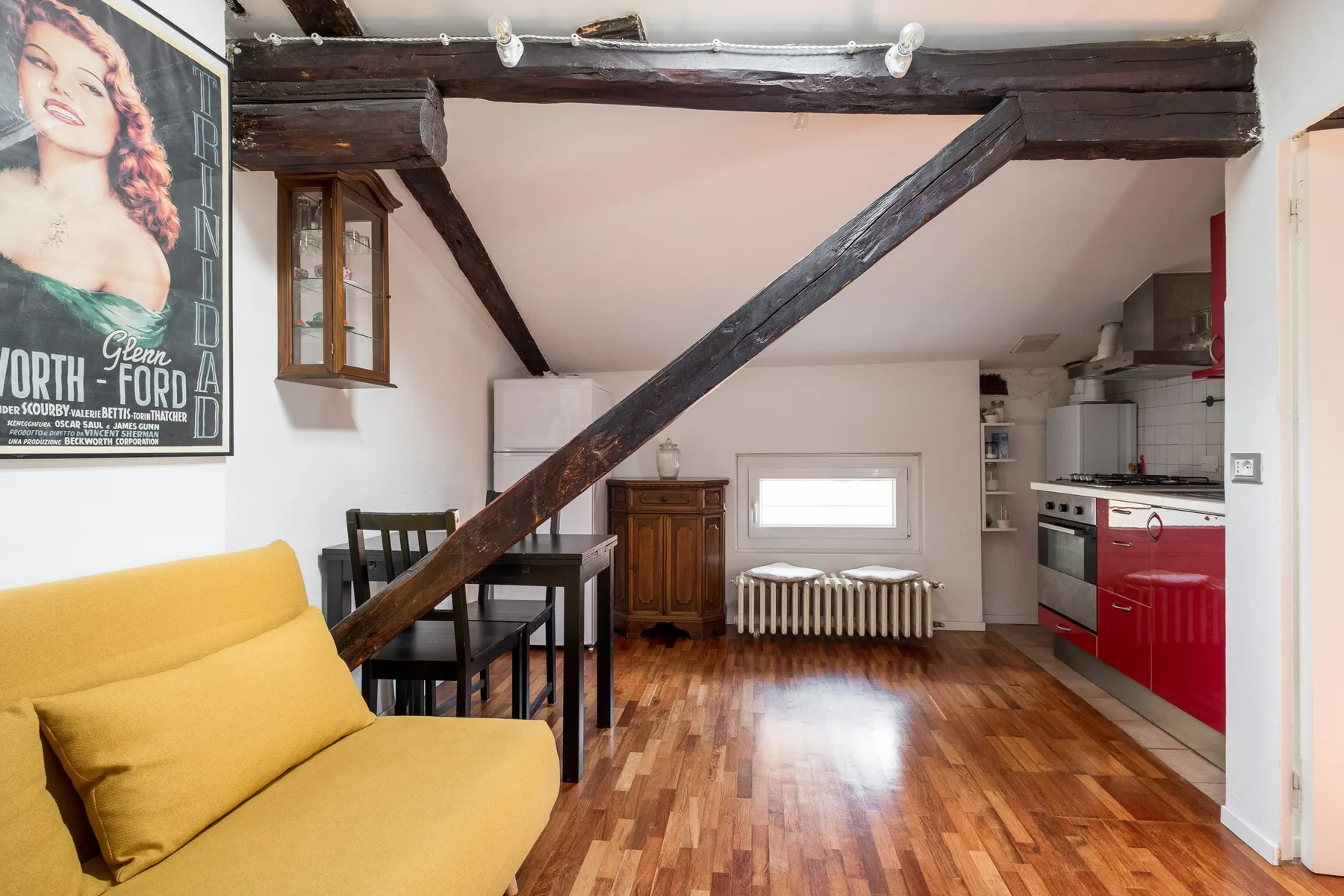 Una pequeña zona de estar con sofá amarillo, mesa de comedor y cocina.