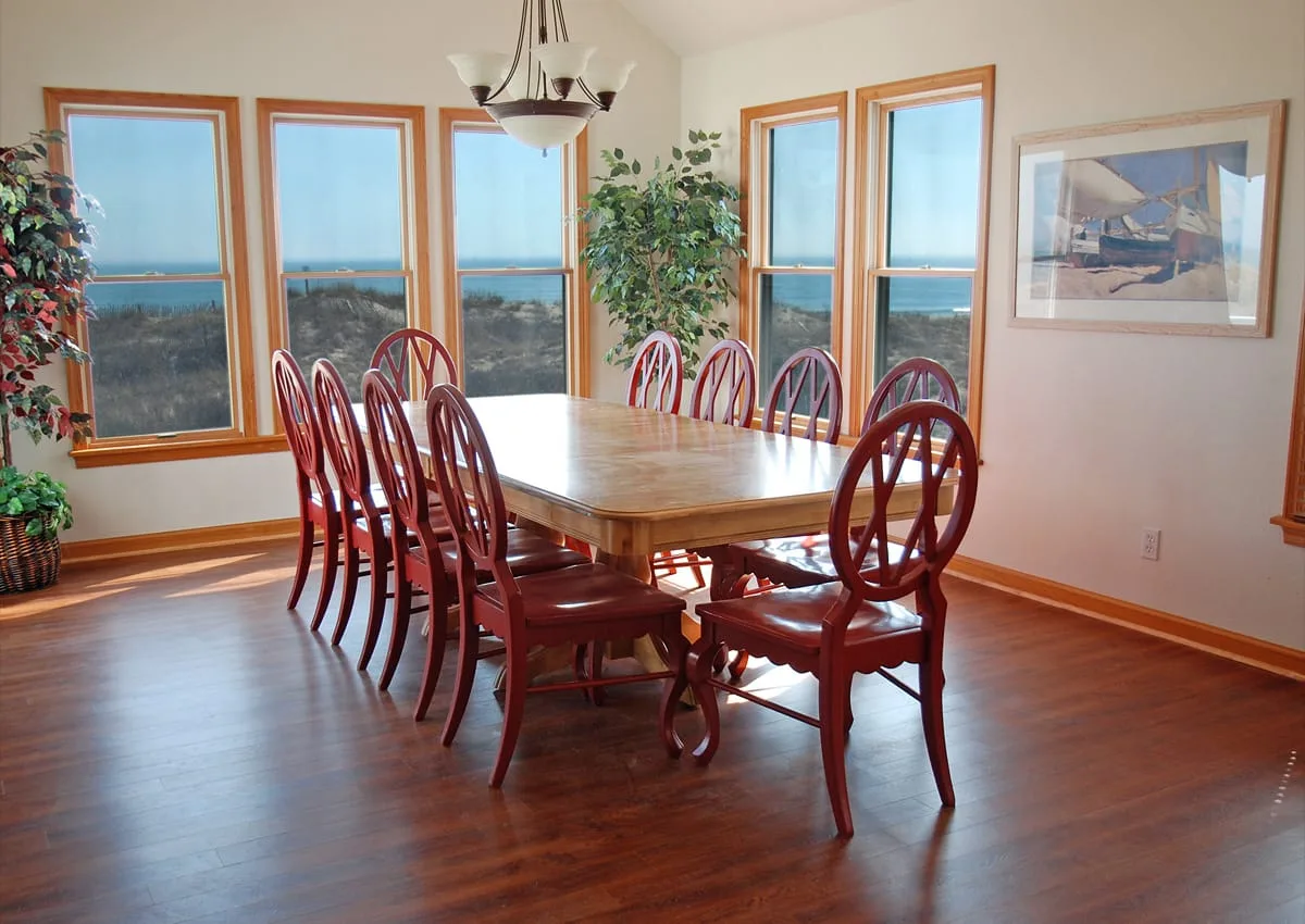 Comedor con una larga mesa de madera y ventanas con vistas al agua.