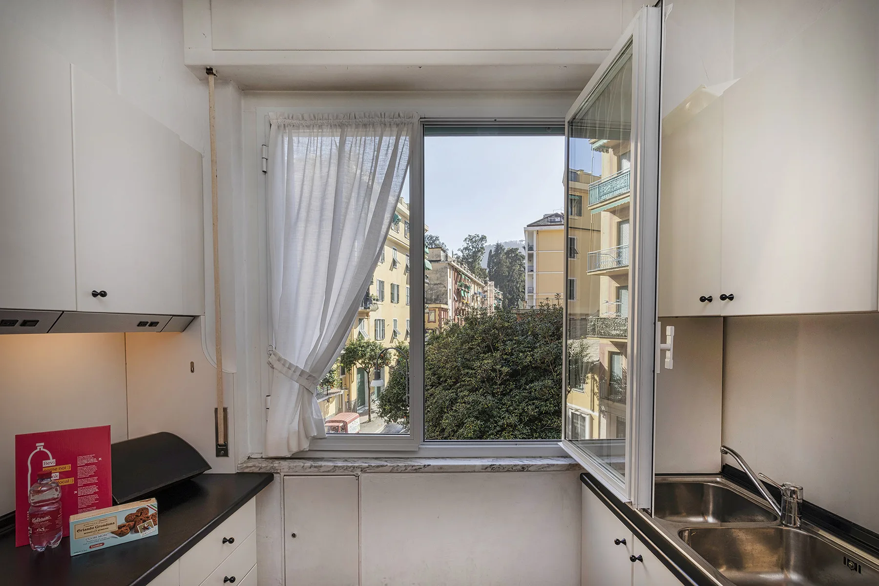 A bright kitchen with white cabinets and a large window overlooking nearby buildings.