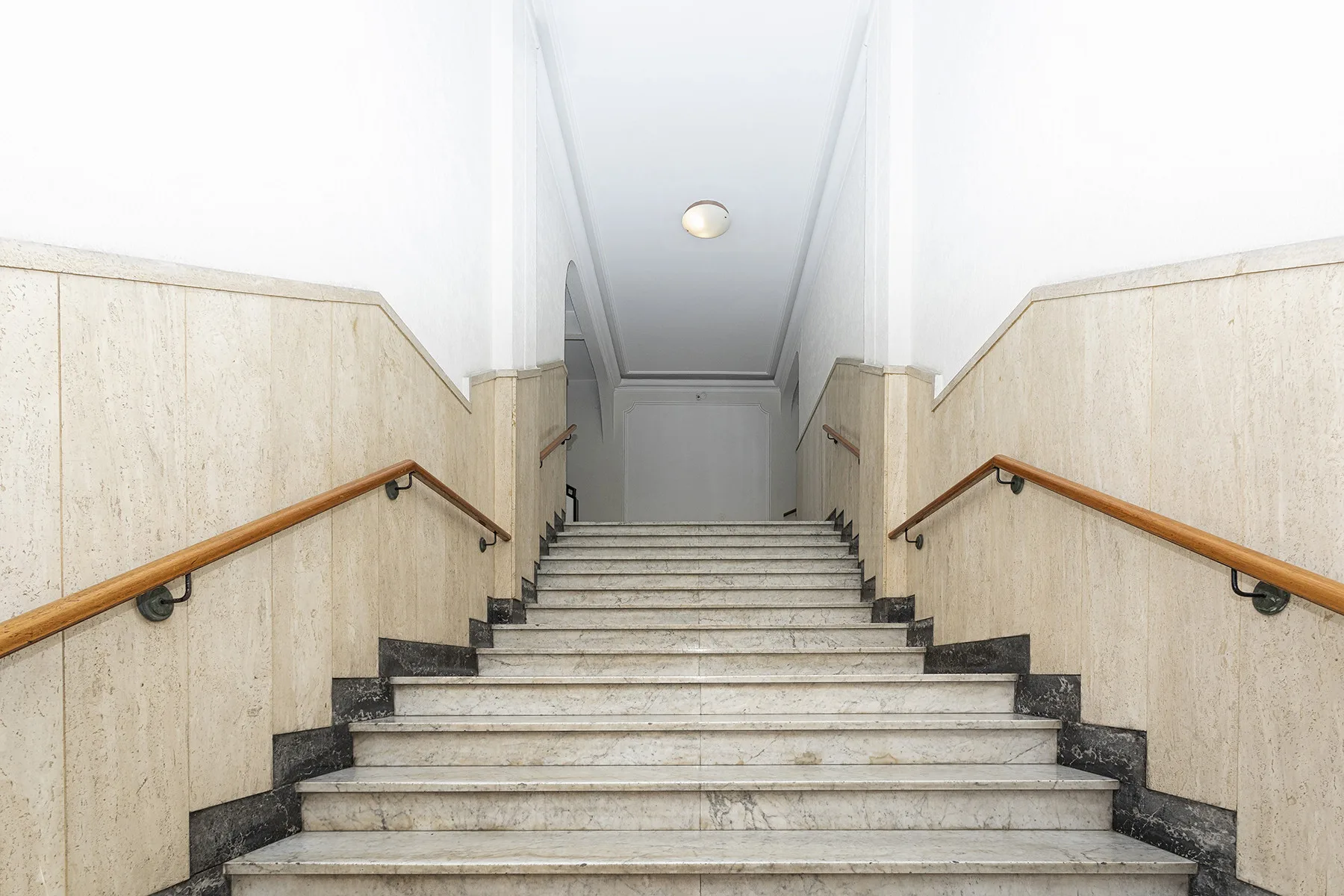 A marble staircase with wooden handrails leads to a landing.