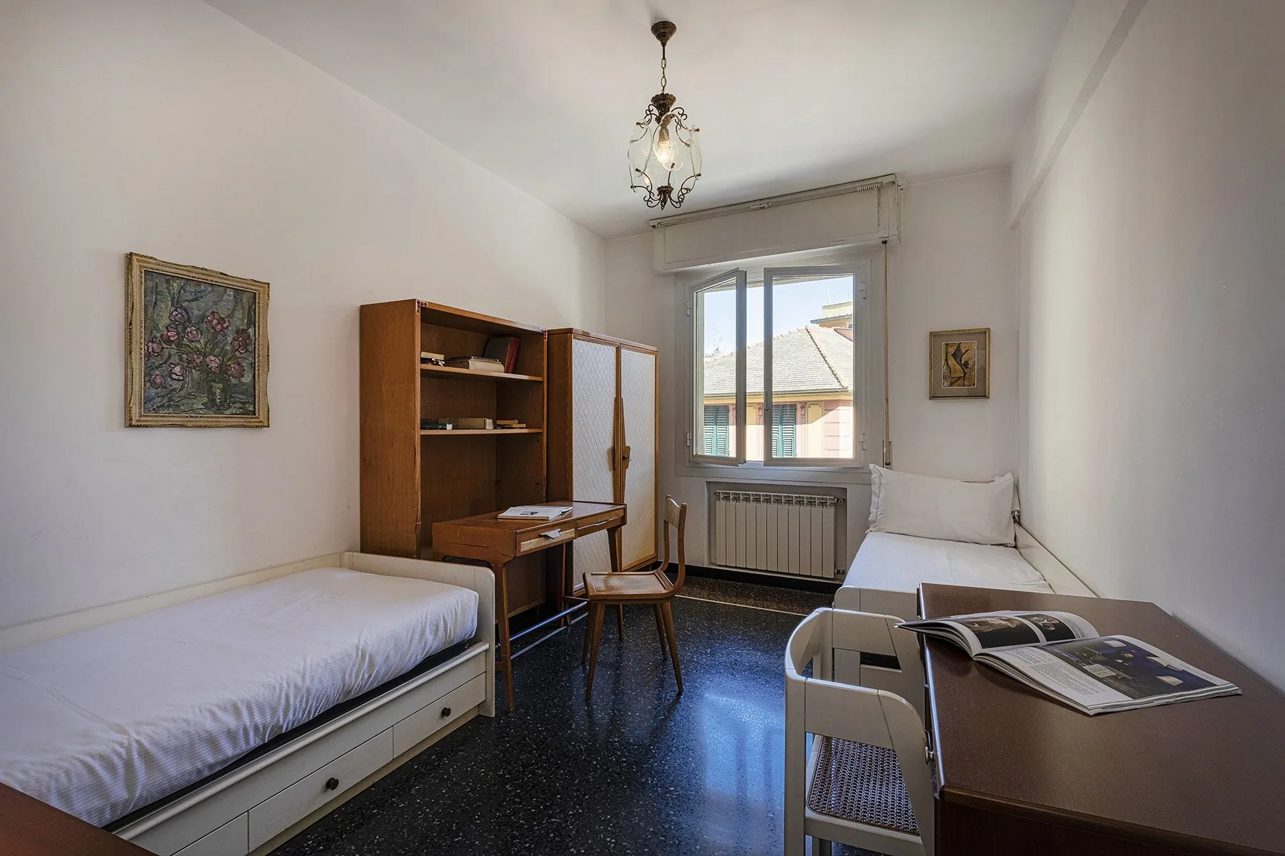 A bright bedroom with two beds, a desk, and a window.