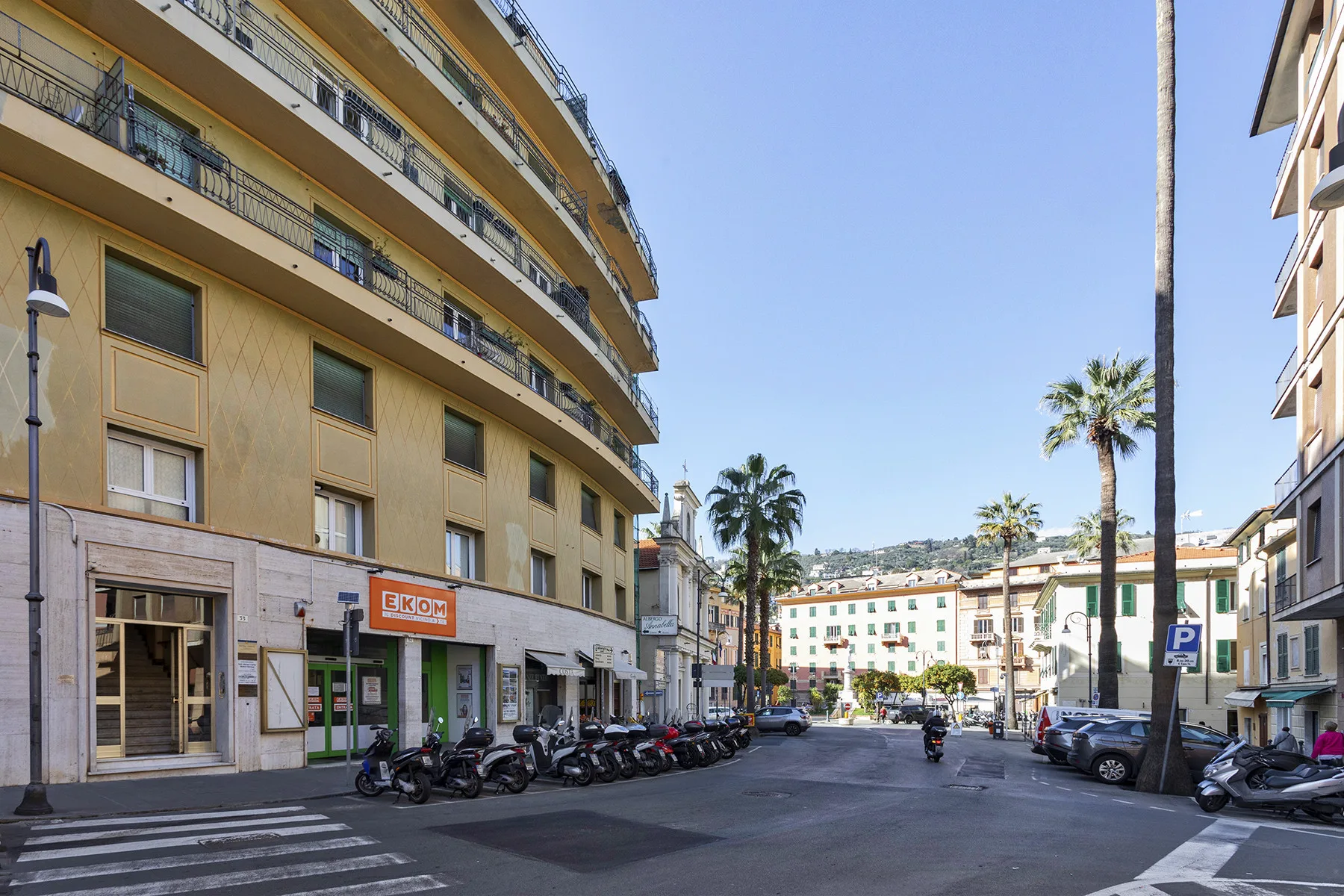 An urban street lined with apartment buildings, parked vehicles, and palm trees.