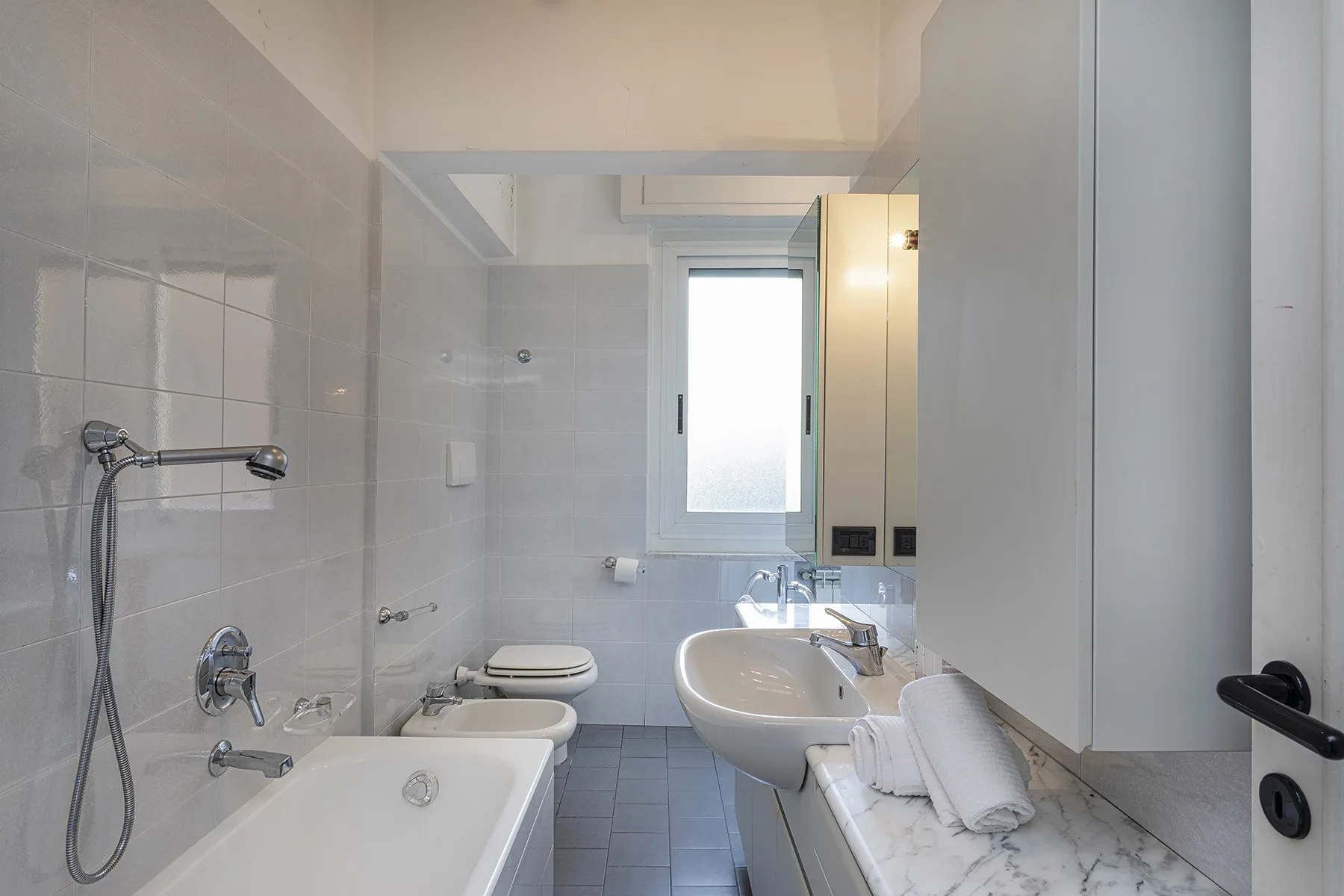 A tiled bathroom with a bathtub, shower fixtures, and a sink.