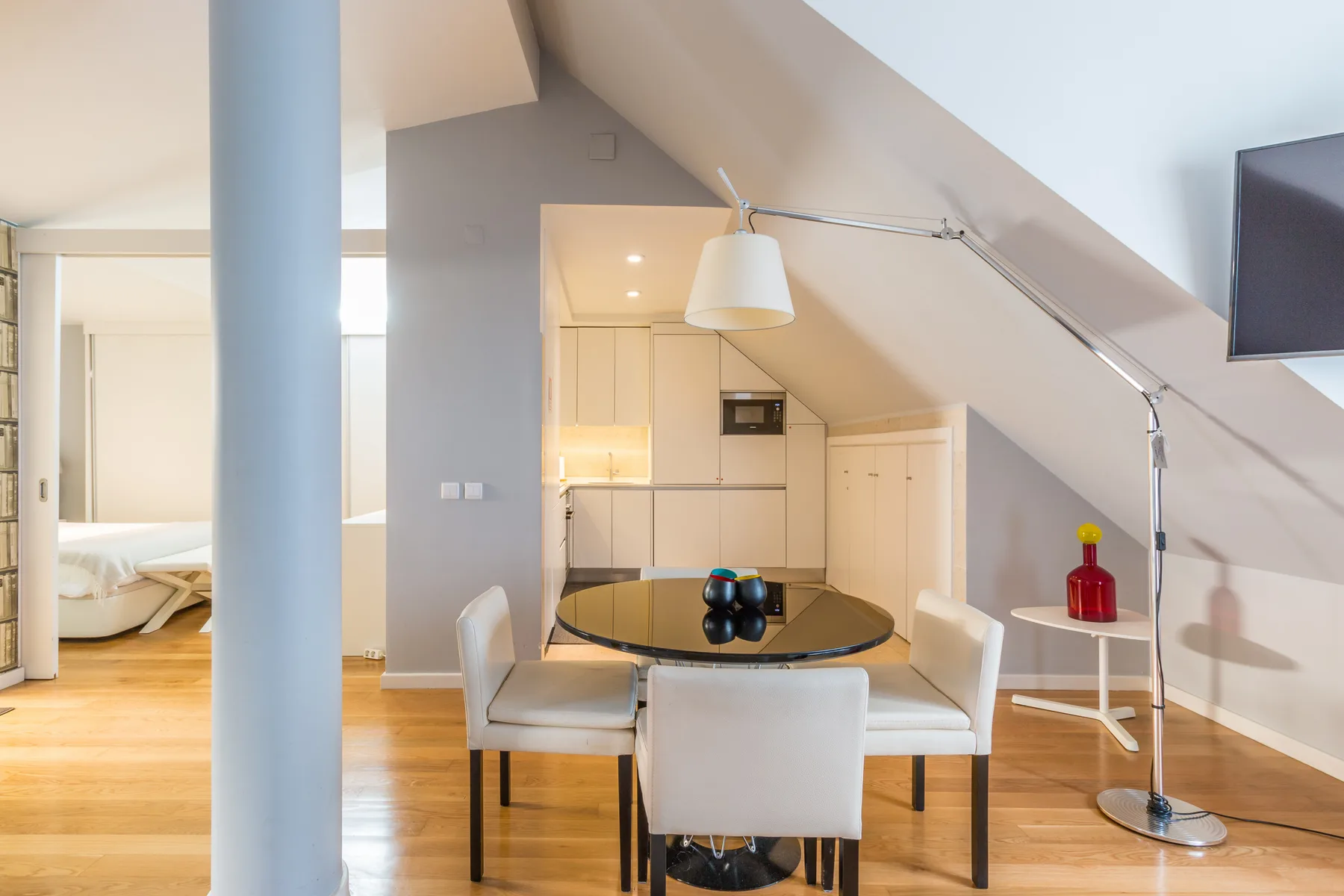Comedor tipo loft con una mesa redonda, asientos claros y una cocina compacta.