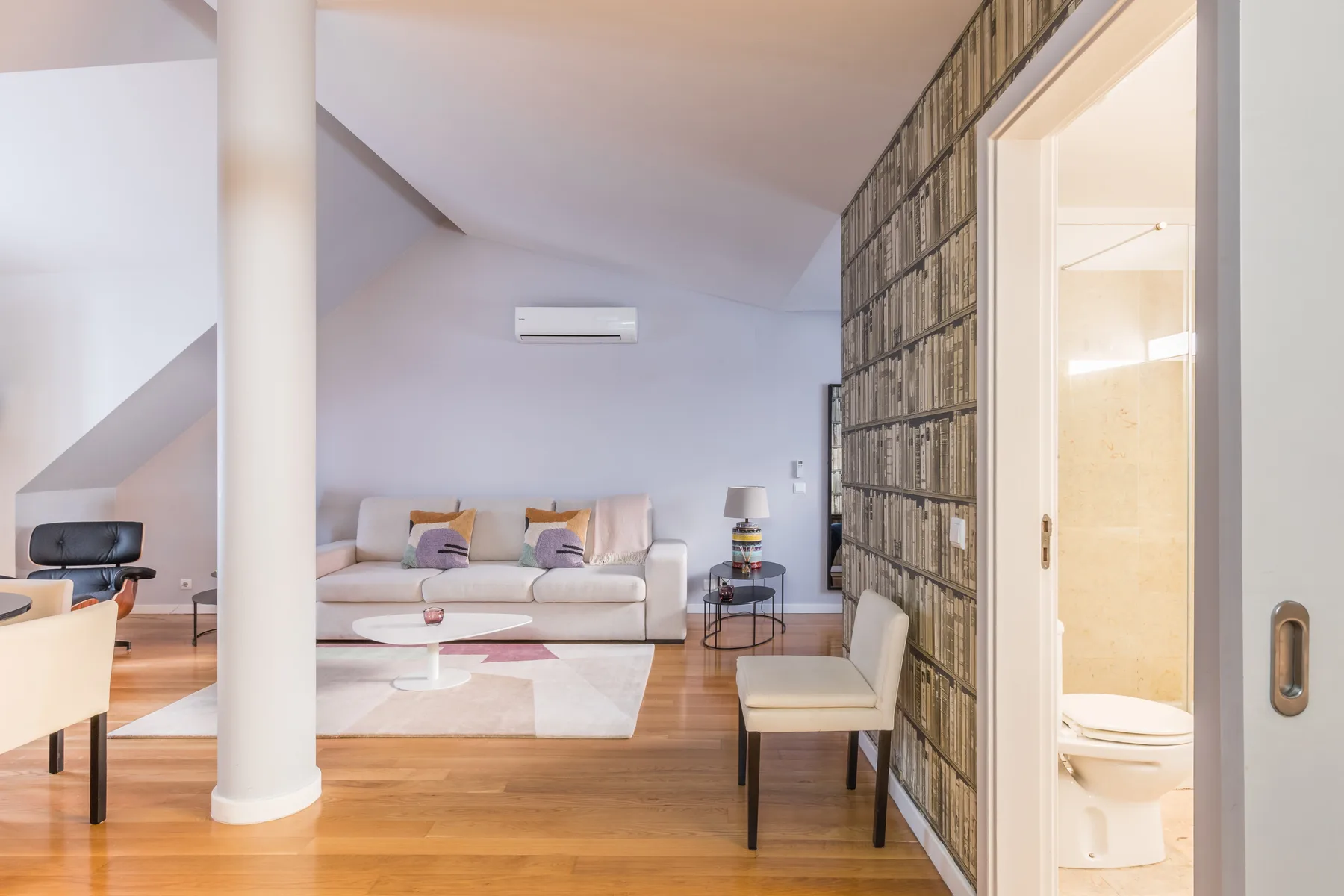 Una sala luminosa con asientos, una mesa de centro y una estantería alta.