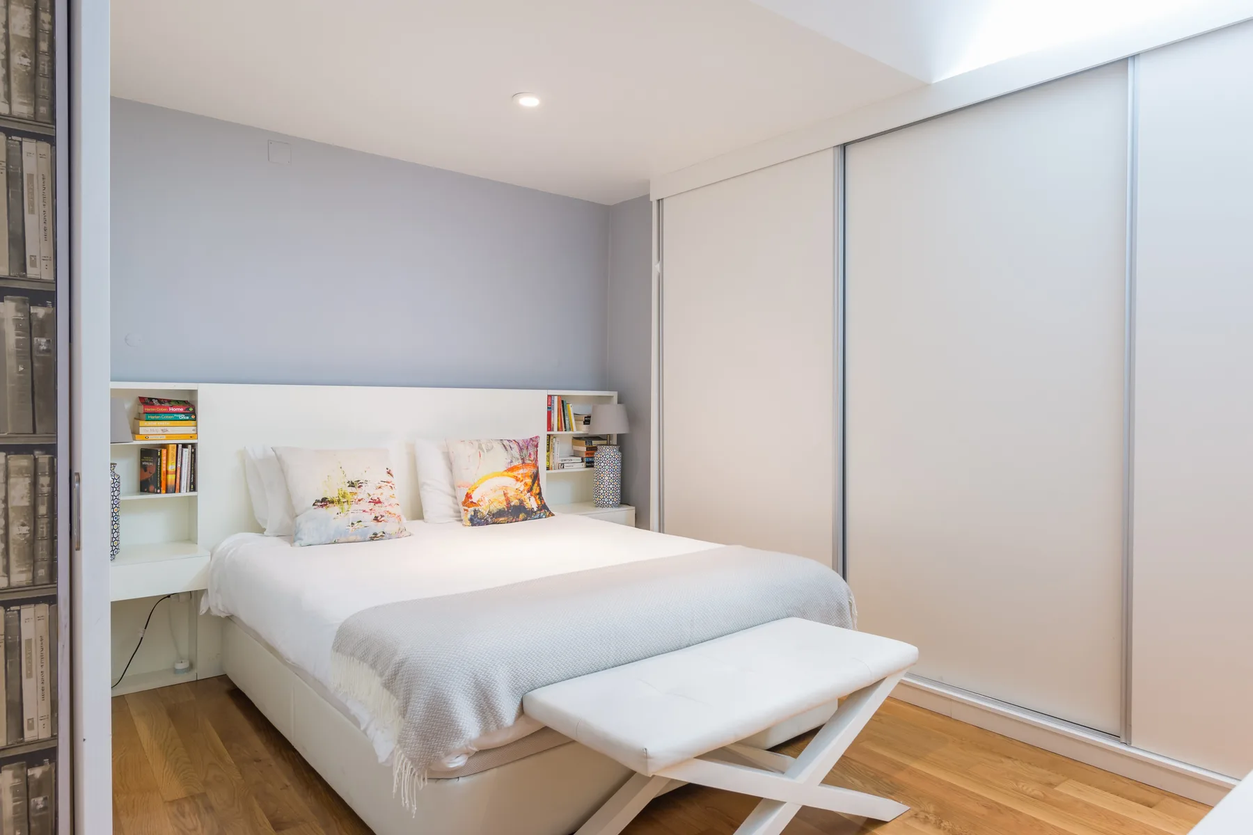 Dormitorio con una cama, un banco y estanterías empotradas.