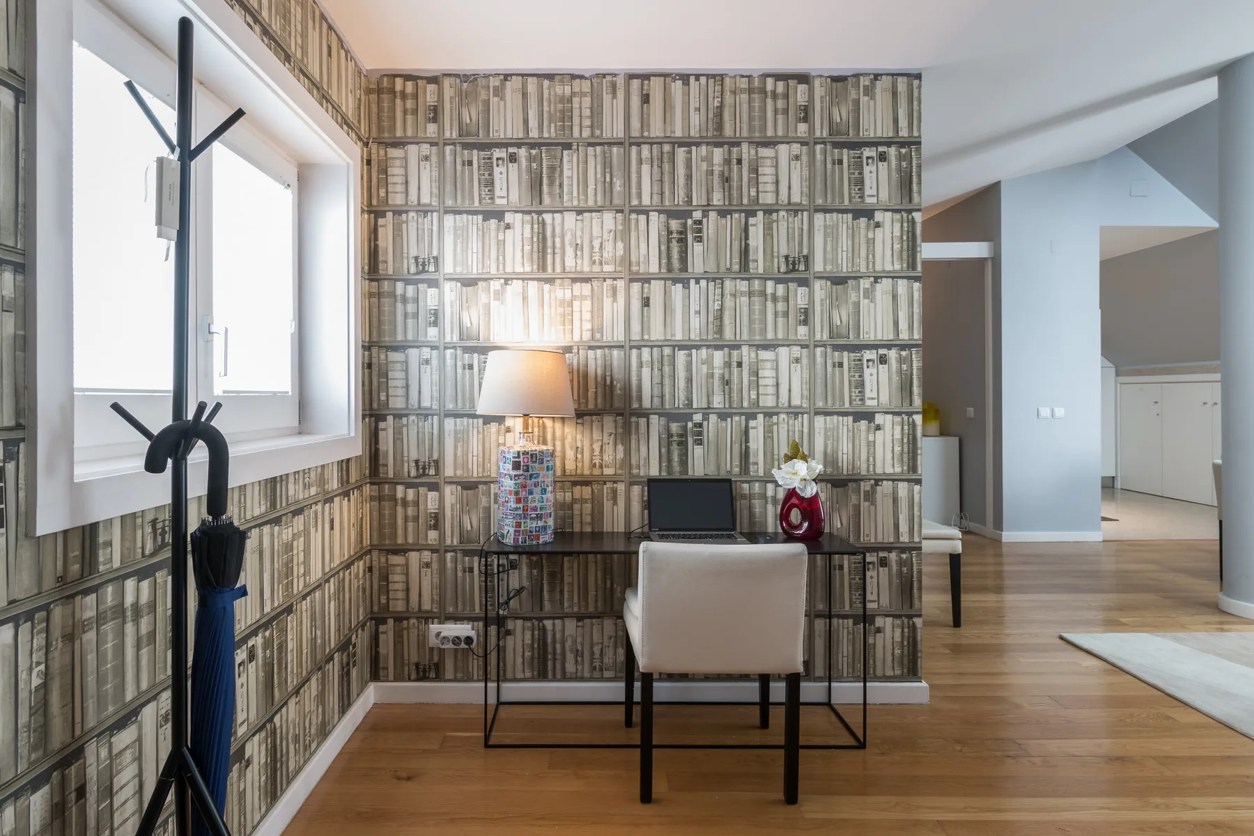 Una sala luminosa cuenta con una pared de estanterías y un escritorio junto a la ventana.