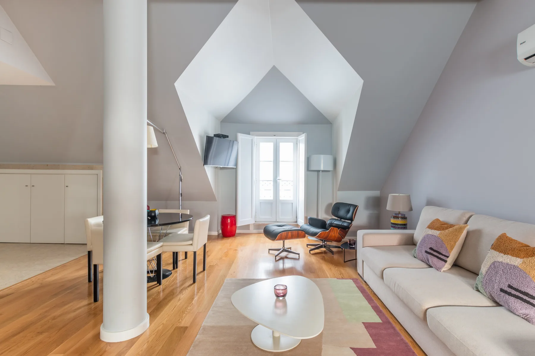 Una luminosa sala de estar tipo loft con asientos, una mesa de centro y ventanas bajo un techo inclinado.