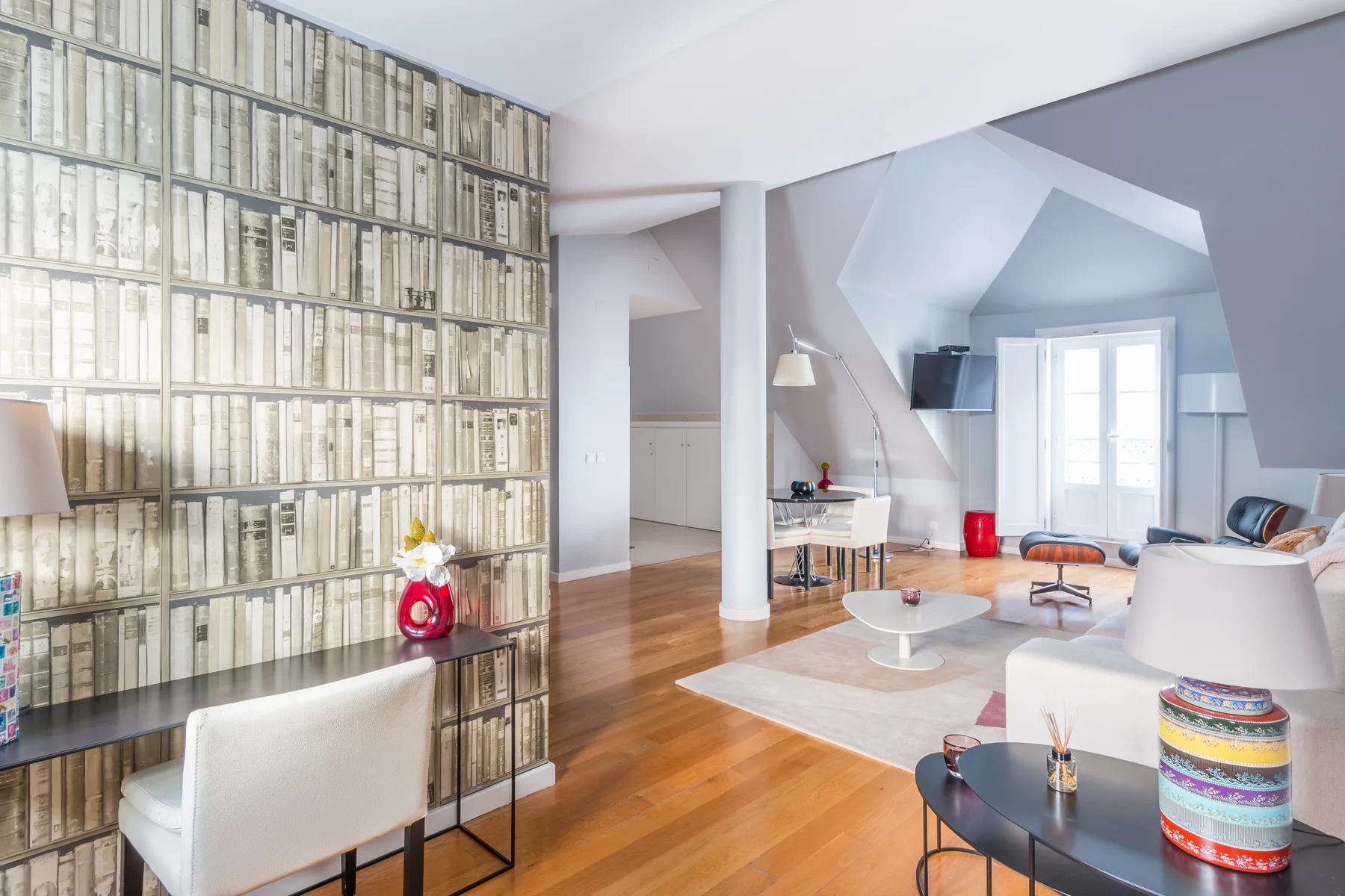 Una sala luminosa con una estantería alta y una zona de estar.
