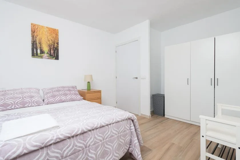 Un dormitorio luminoso con una cama, armarios blancos y un cuadro en la pared.