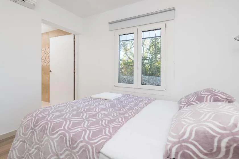 Un dormitorio luminoso con ropa de cama estampada y una ventana con vistas a los árboles.