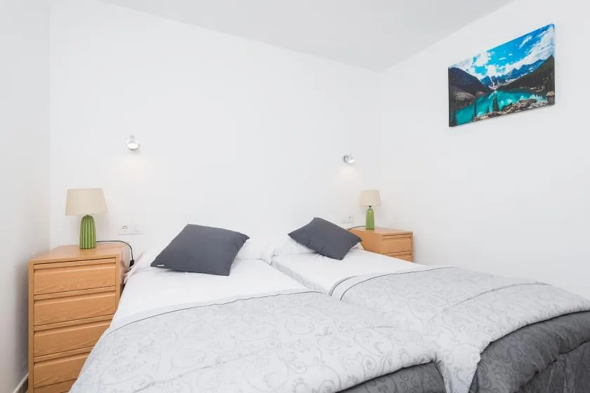 Un dormitorio luminoso con dos camas, cómodas de madera y una imagen de montañas.