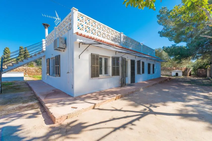 Una casa blanca con una terraza sombreada se encuentra bajo un cielo azul brillante.