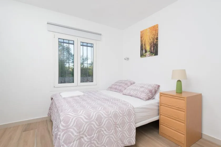 Un dormitorio con una cama junto a una ventana y una cómoda de madera.
