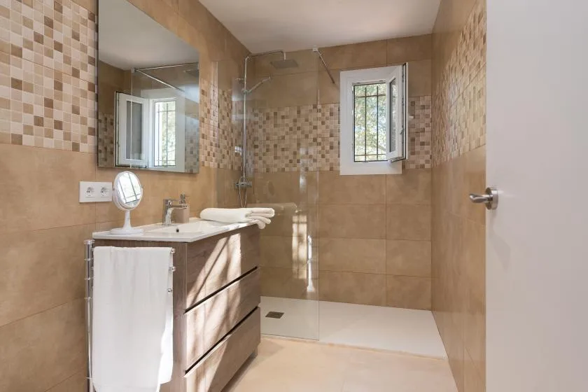 Baño alicatado con lavabo, espejo y ducha de cristal.