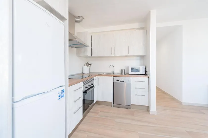 Una cocina luminosa con gabinetes blancos, un refrigerador y electrodomésticos de acero inoxidable.