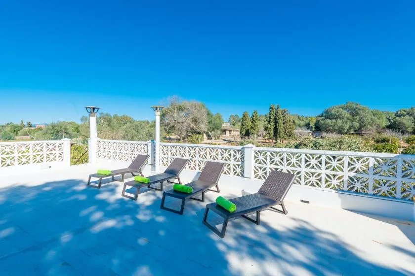 Una terraza soleada con tumbonas reclinables junto a una barandilla blanca decorativa.