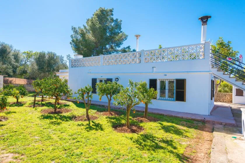 Una casa blanca se encuentra junto a un jardín soleado con árboles y césped verde.