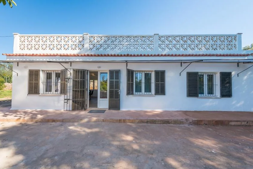 Un edificio blanco de una planta con ventanas con postigos y una barandilla en la terraza.