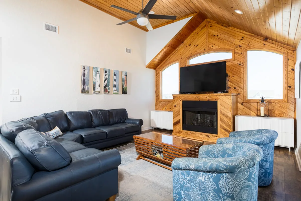 Una sala de estar con asientos oscuros, una pared de madera con chimenea y un televisor.