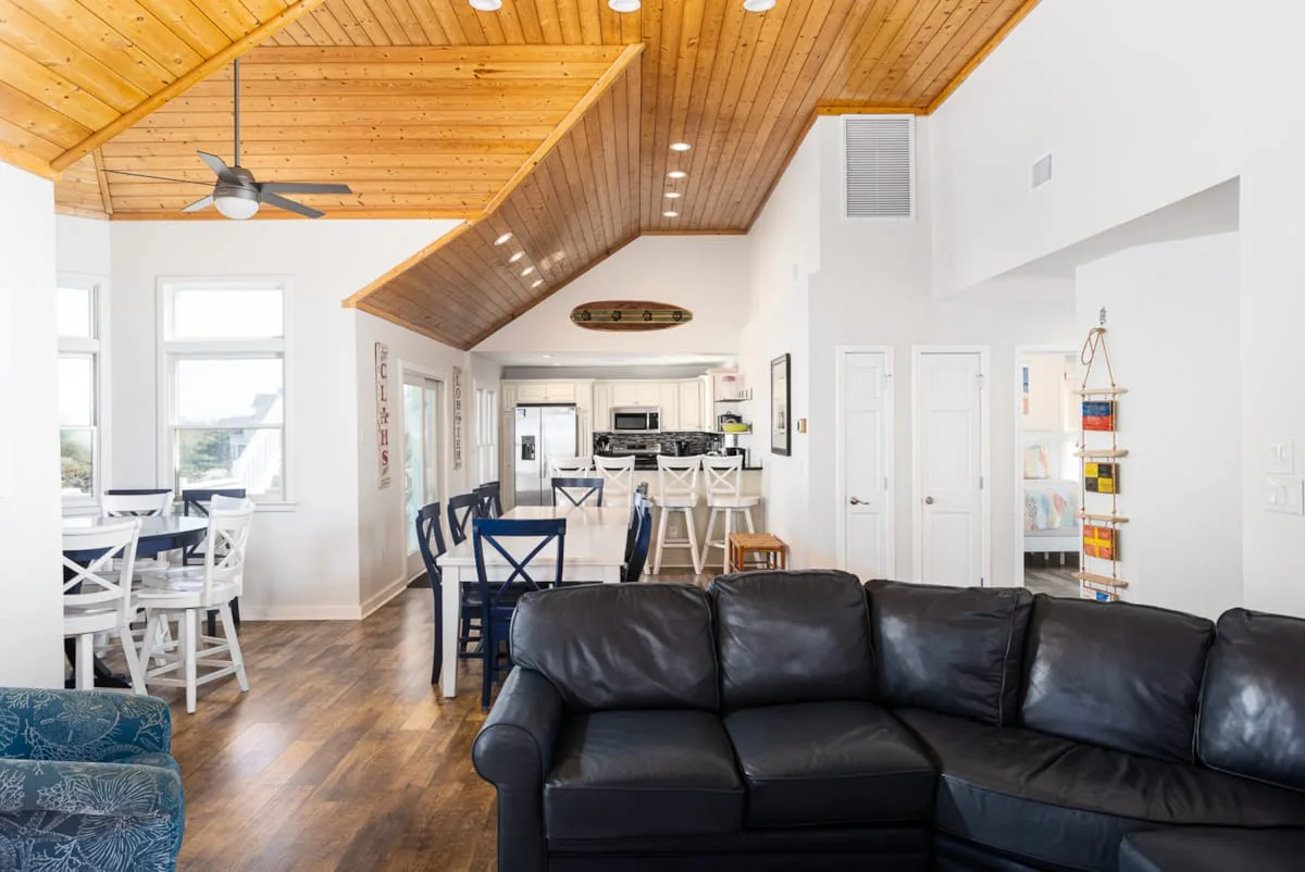 Una sala y comedor abiertos con asientos oscuros bajo un techo revestido de madera.