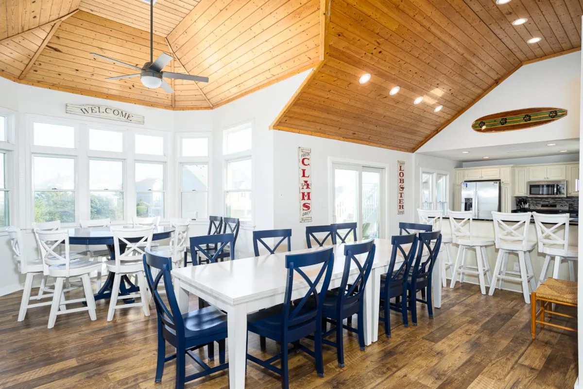 Comedor con mesas blancas y asientos azules y blancos bajo un techo revestido de madera.
