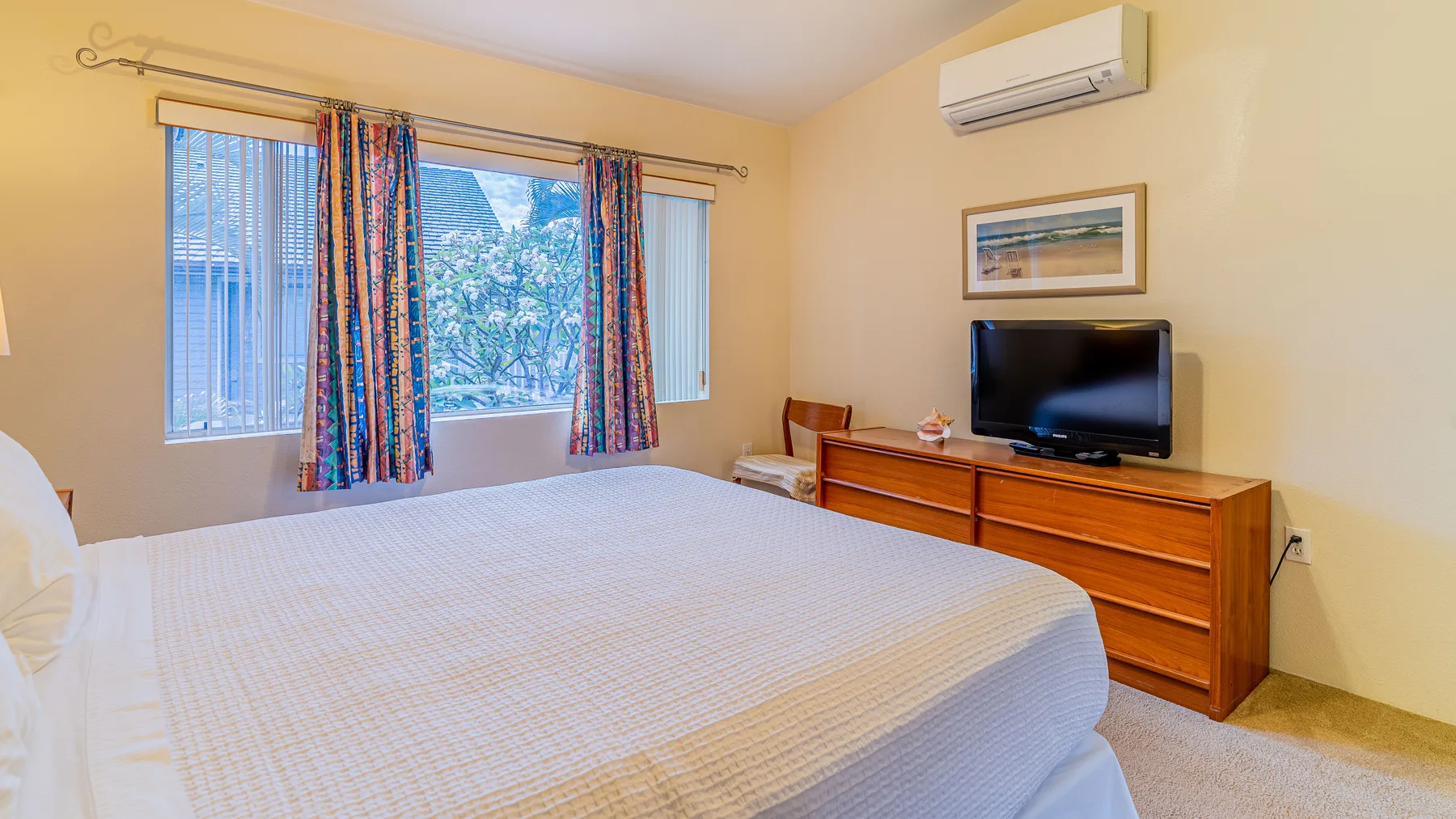 A bedroom with a large bed, curtained windows, and a television on a dresser.