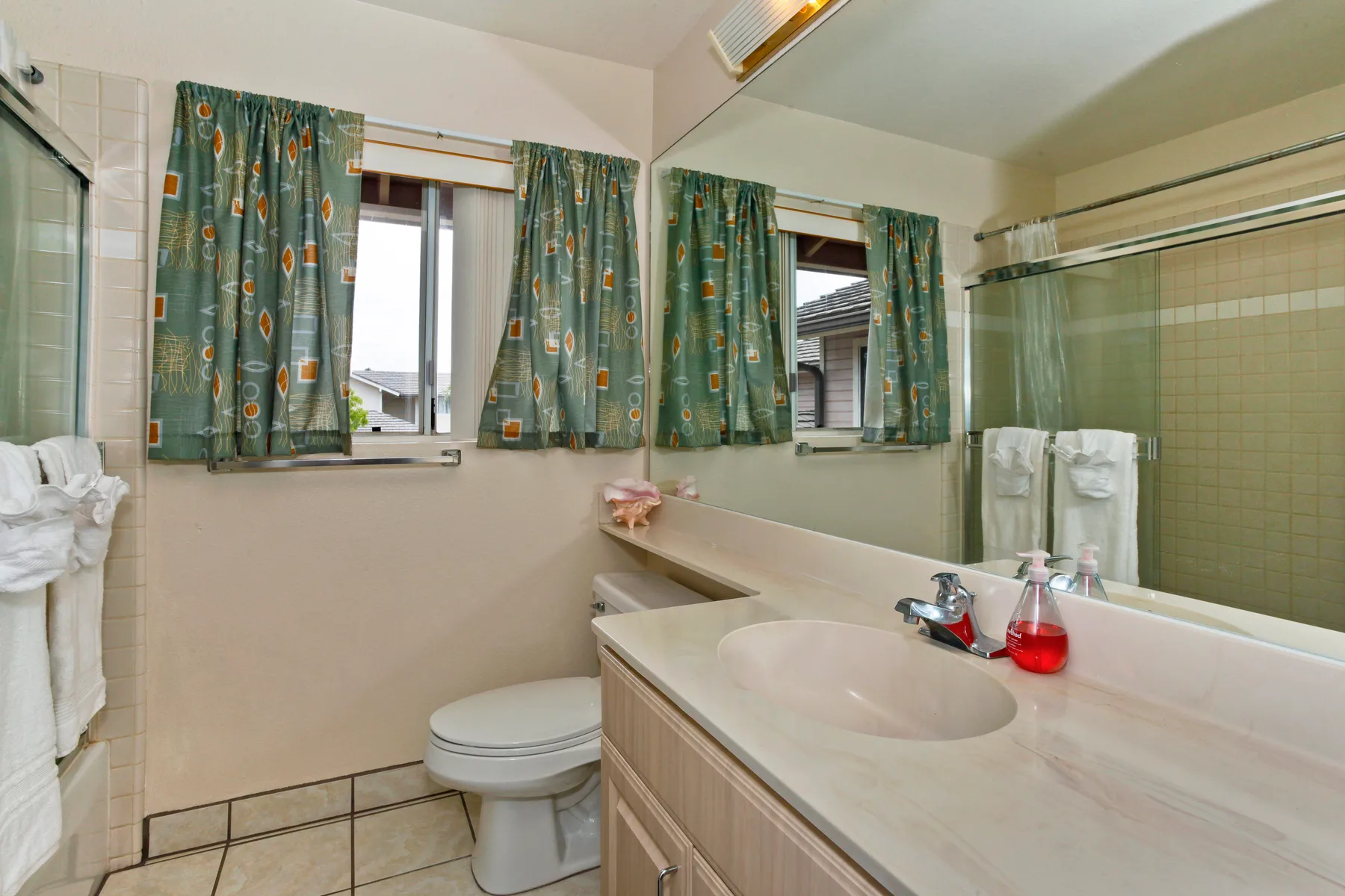 A bathroom with a sink, toilet, and windows with patterned curtains.